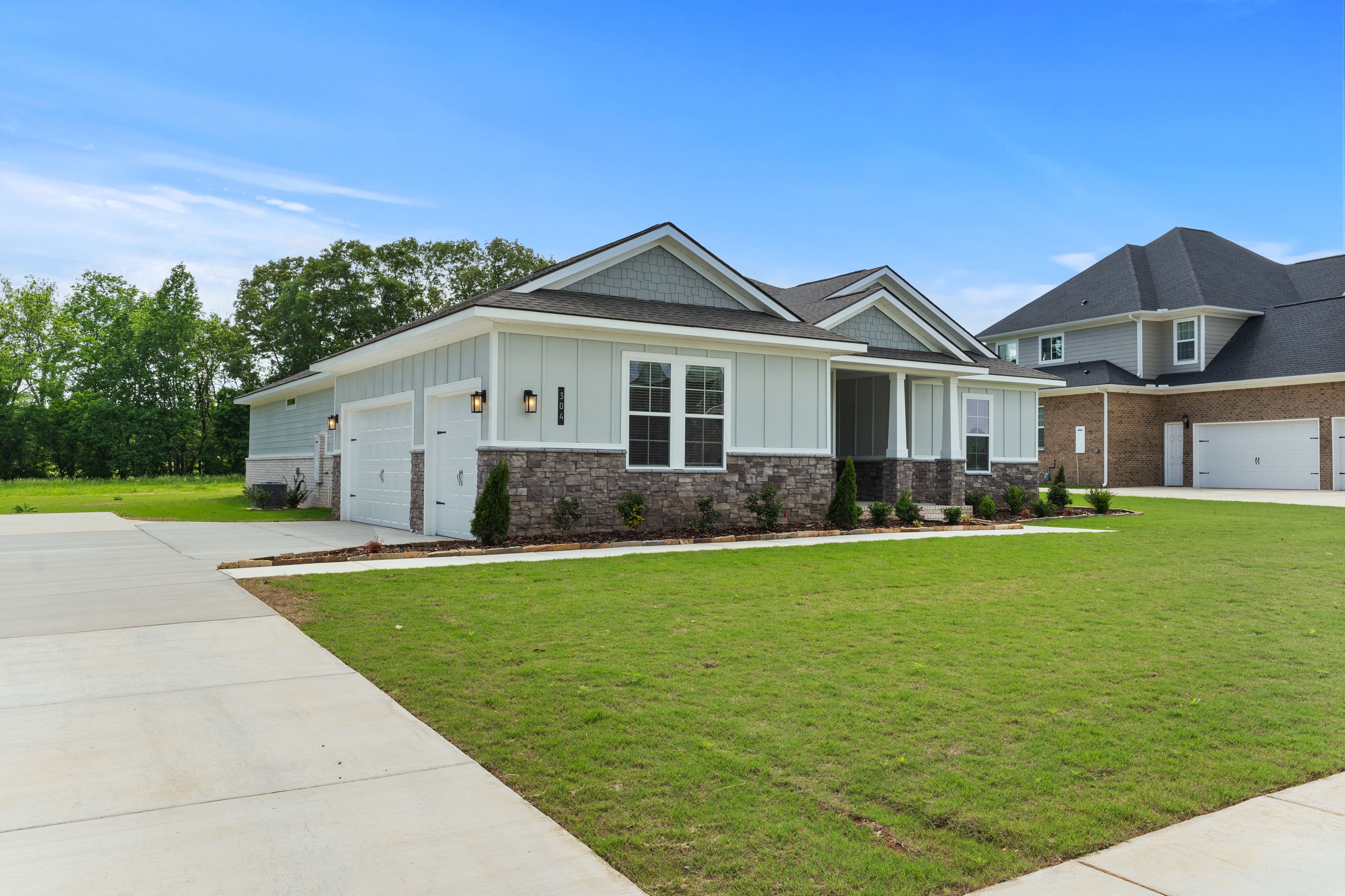 Modern single-story exterior of The Arcadia B with 3-car garage, gray siding, stone accents, and manicured lawn in Owens Cross Roads