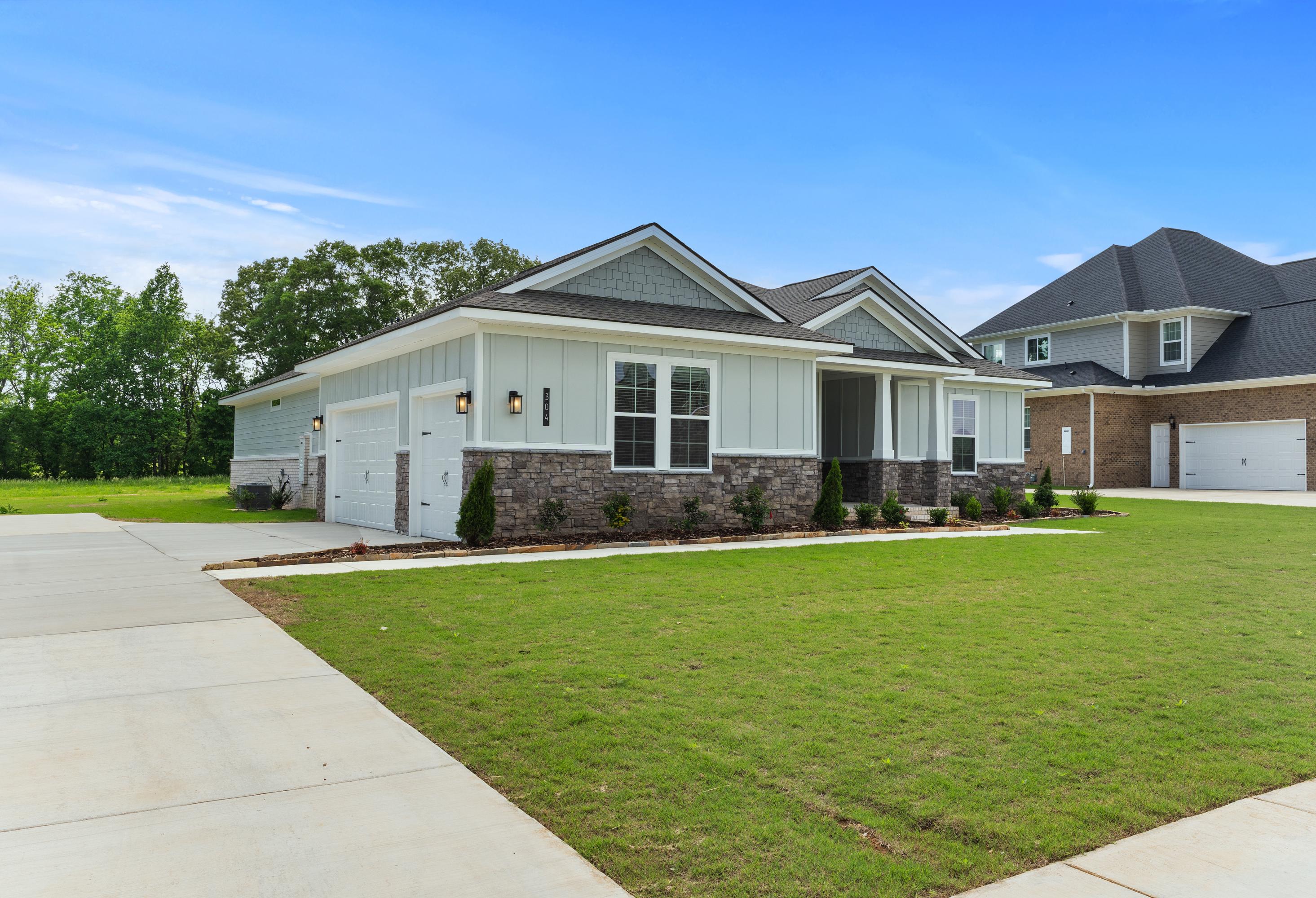 Modern single-story exterior of The Arcadia B with 3-car garage, gray siding, stone accents, and manicured lawn in Owens Cross Roads