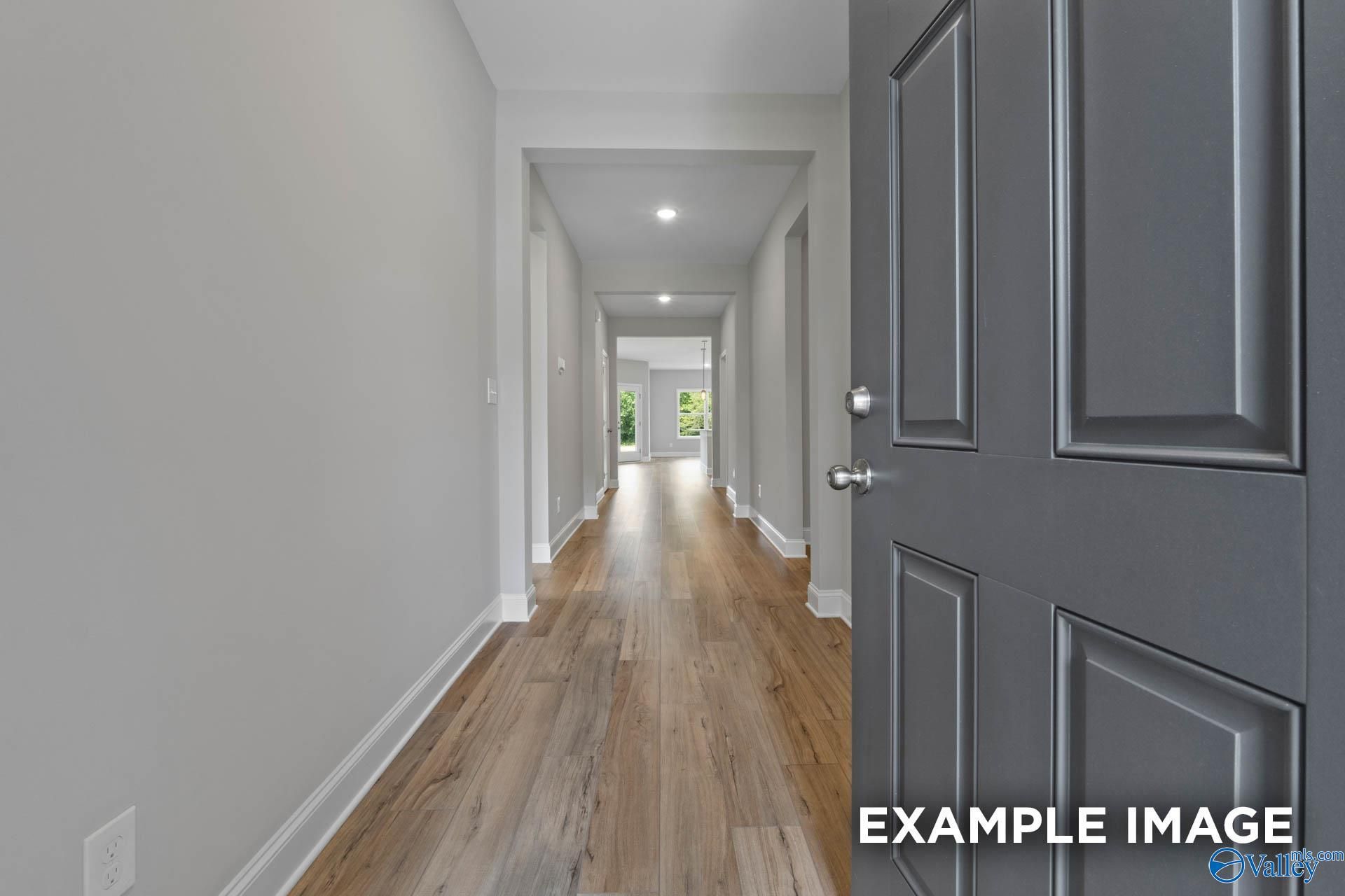 Long hallway with light oak flooring, gray walls, and open doors in The Everett B 4-bedroom home, Athens, Alabama