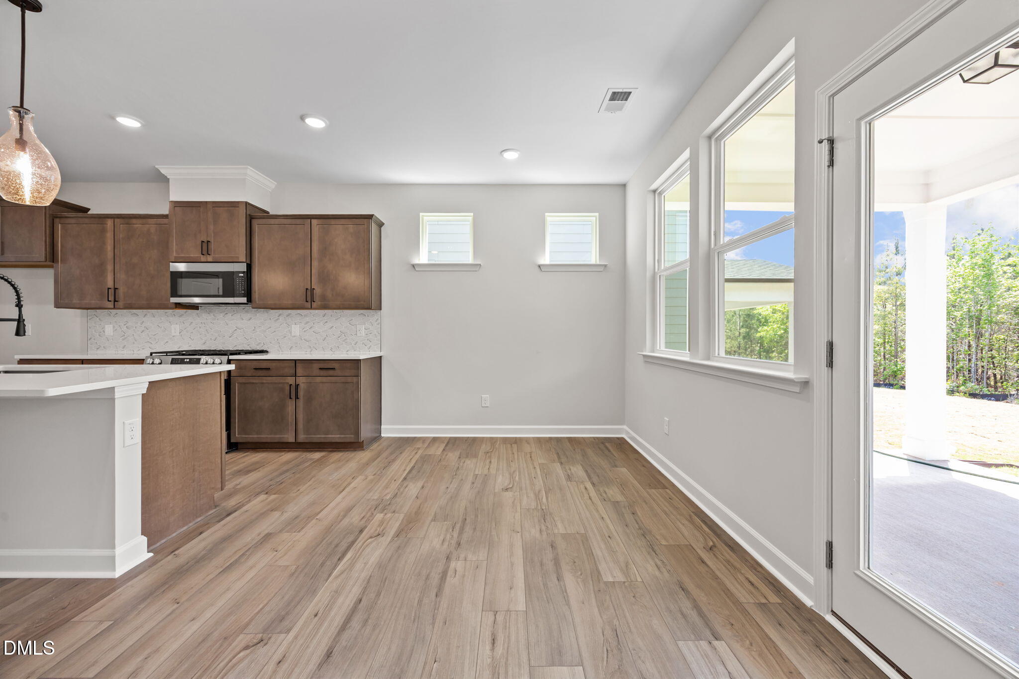 Modern open-concept kitchen with white quartz island, shaker cabinets, stainless appliances, and sliding doors to covered patio in The Willow D, Wendell, NC
