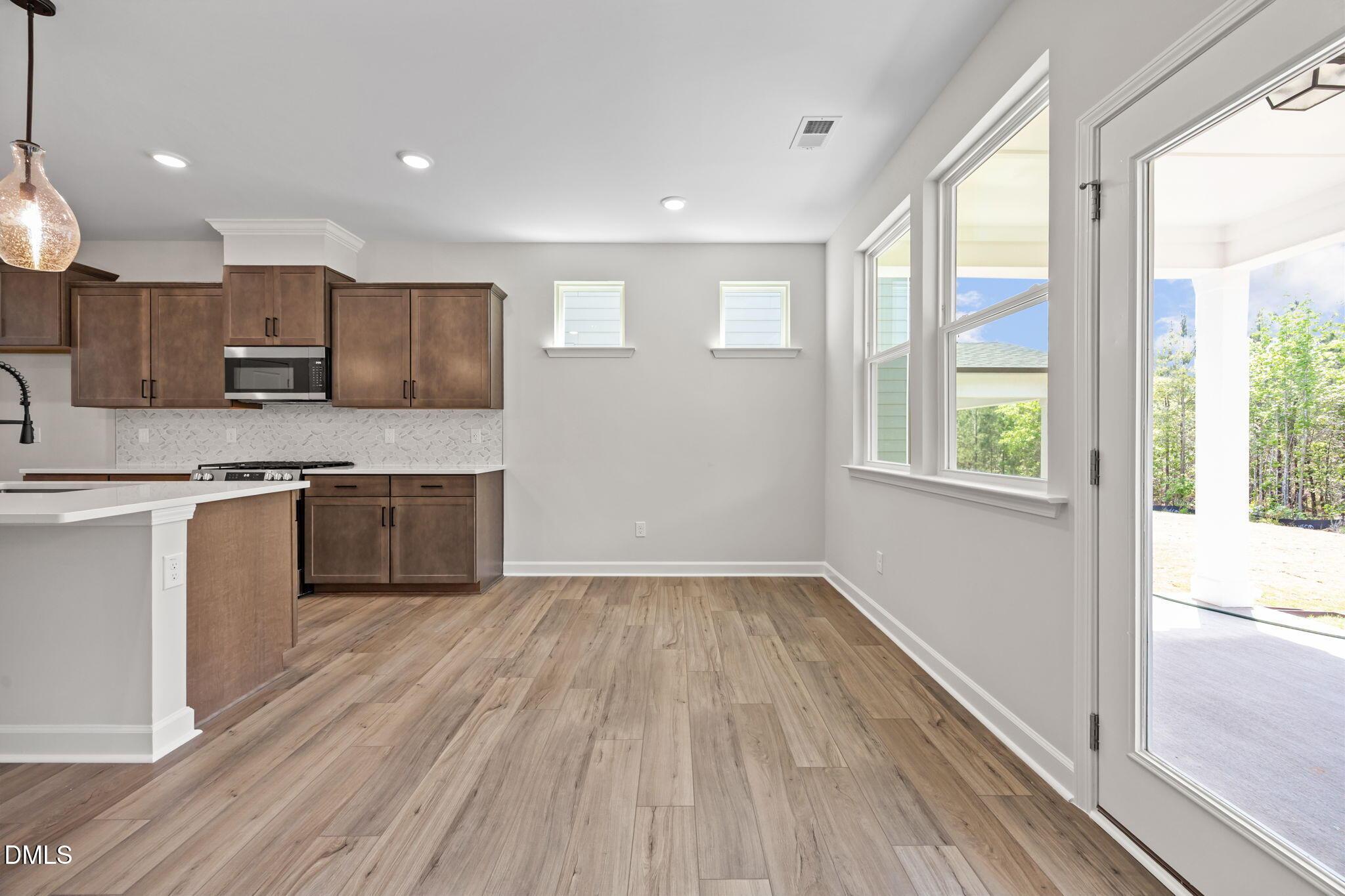 Modern open-concept kitchen with white quartz island, shaker cabinets, stainless appliances, and sliding doors to covered patio in The Willow D, Wendell, NC