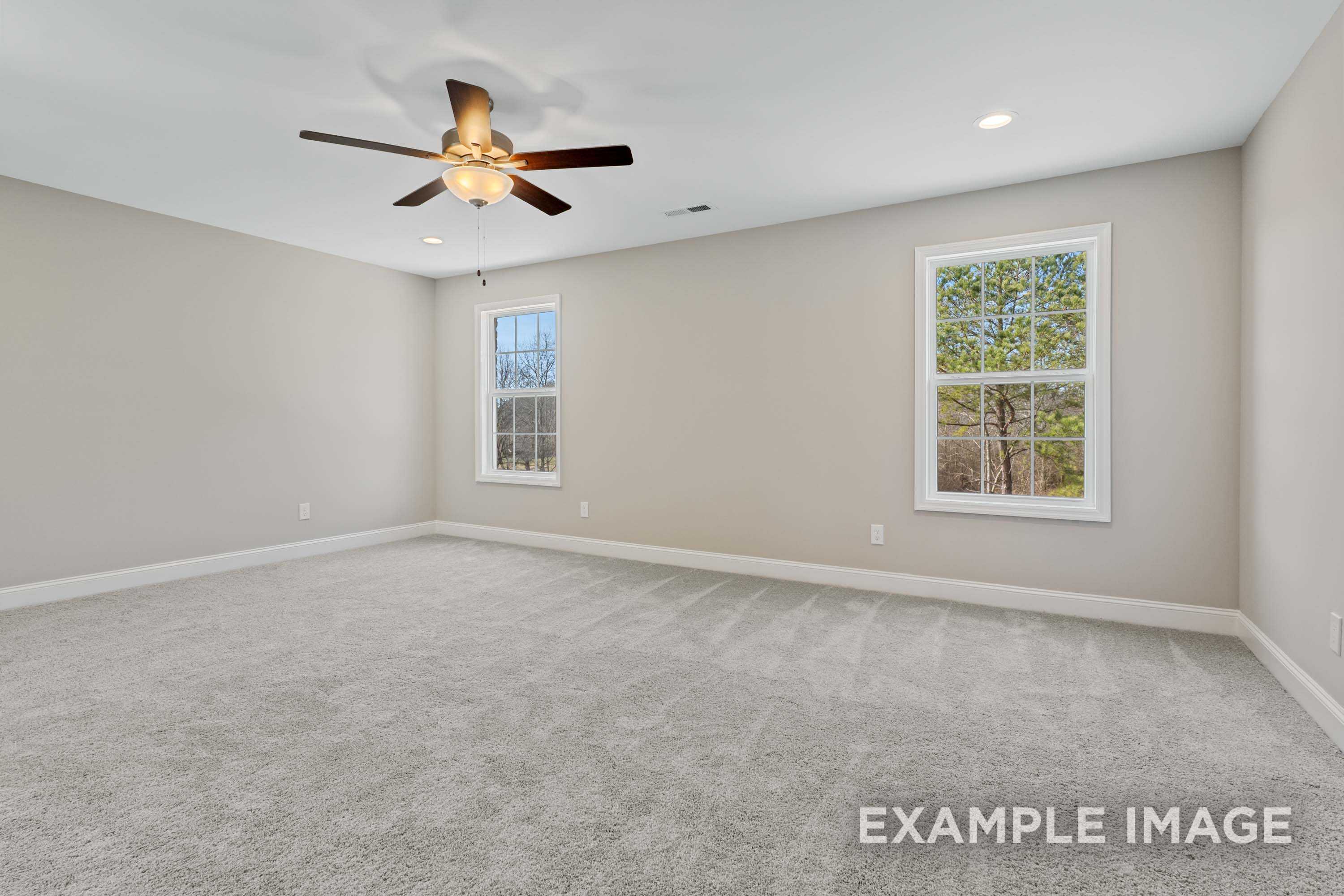 Spacious upstairs bedroom in The Madison A with beige walls, gray carpet, ceiling fan, and large windows