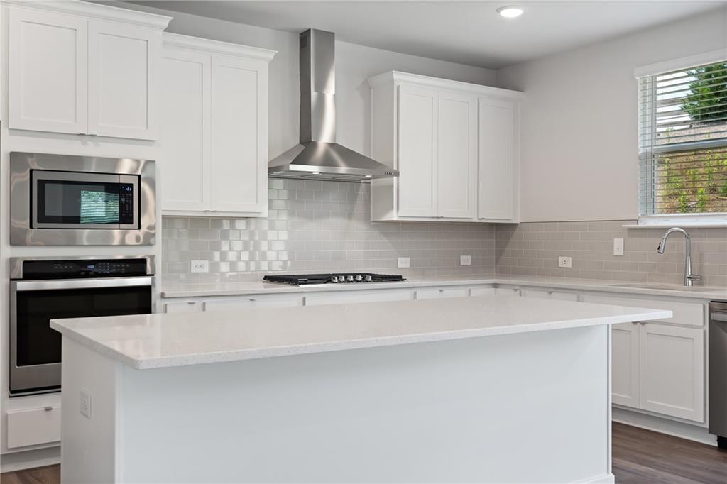 Modern white kitchen with stainless appliances, quartz island, subway tile backsplash in Davidson Homes The Hickory A, Winder, GA