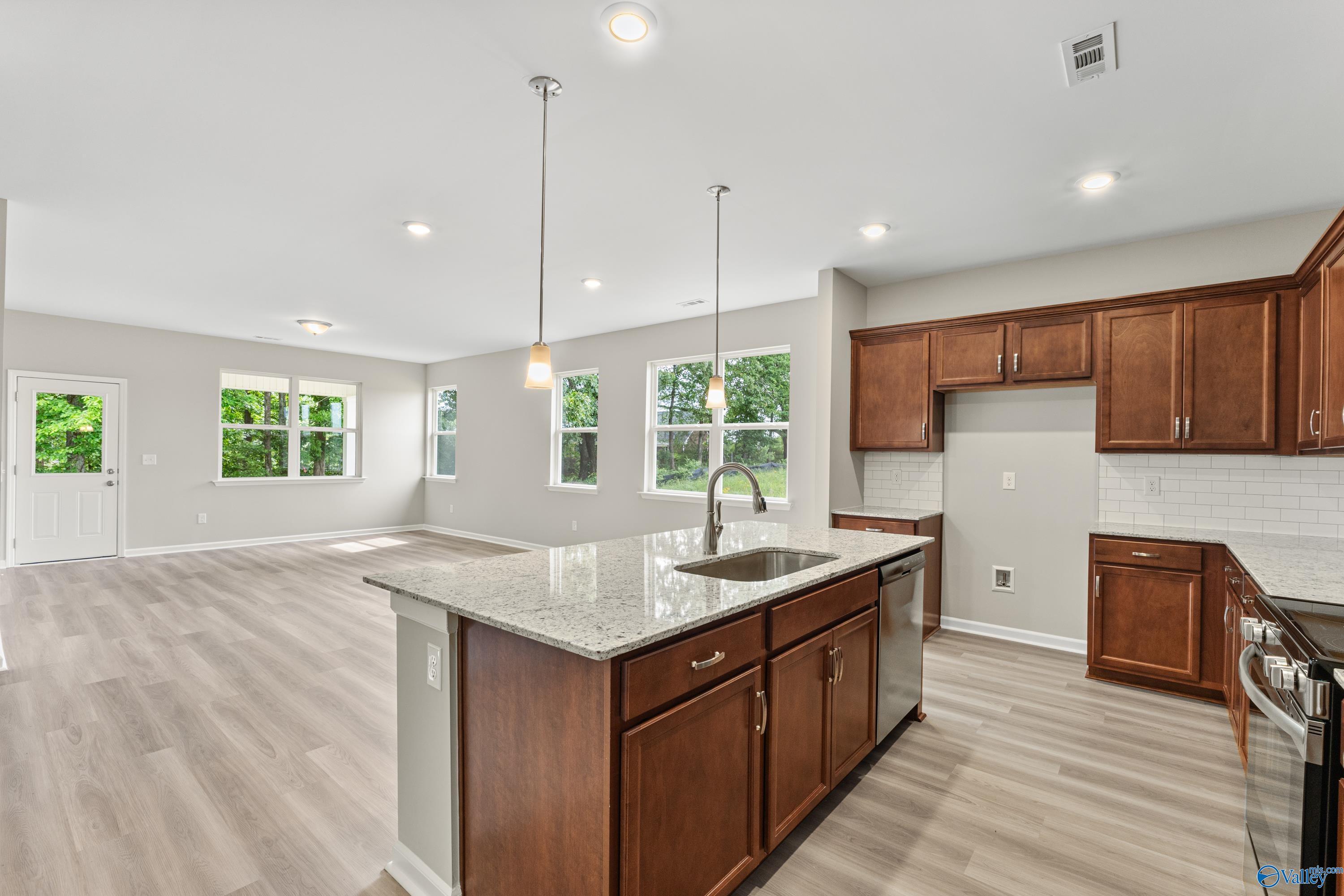 Open-concept kitchen featuring granite island, stainless sink, and wood cabinets in The Aurora floor plan, Fayetteville, TN