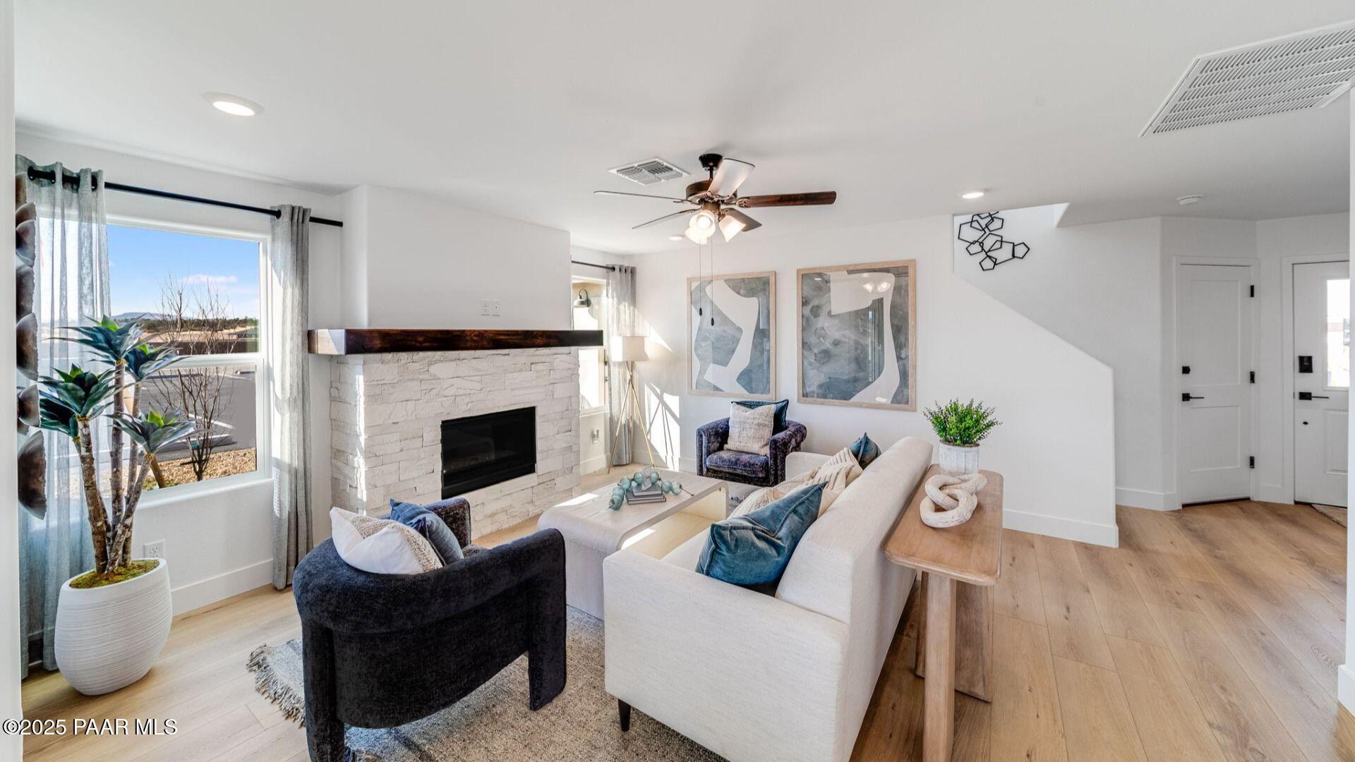 Cozy living room with stone fireplace, plush white sofa, blue abstract art, plants, and large windows in Davidson Homes The Wilmington B, Prescott, Arizona