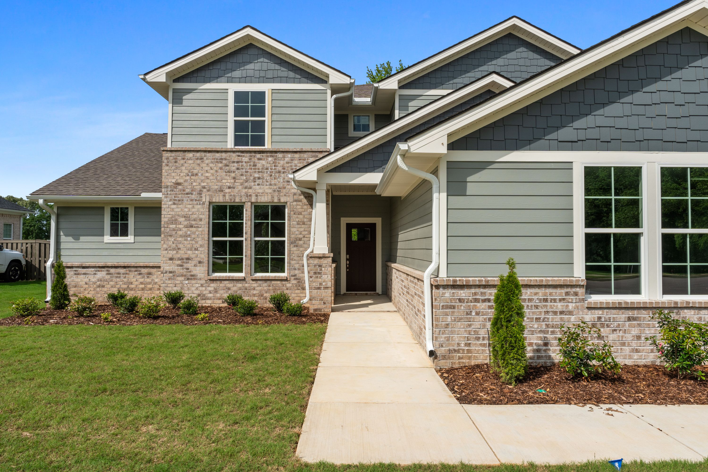 Two-story Avalon E home elevation with gray siding, brick accents, covered porch, and landscaped front yard by Evermore Homes