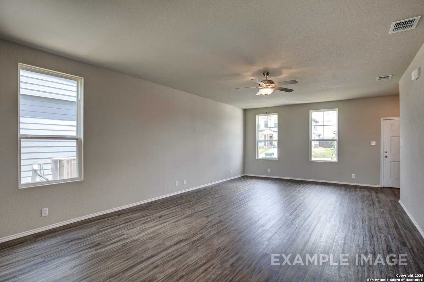Spacious empty living room with hardwood floors, large windows, and ceiling fan in Davidson Homes The Murray K, San Antonio