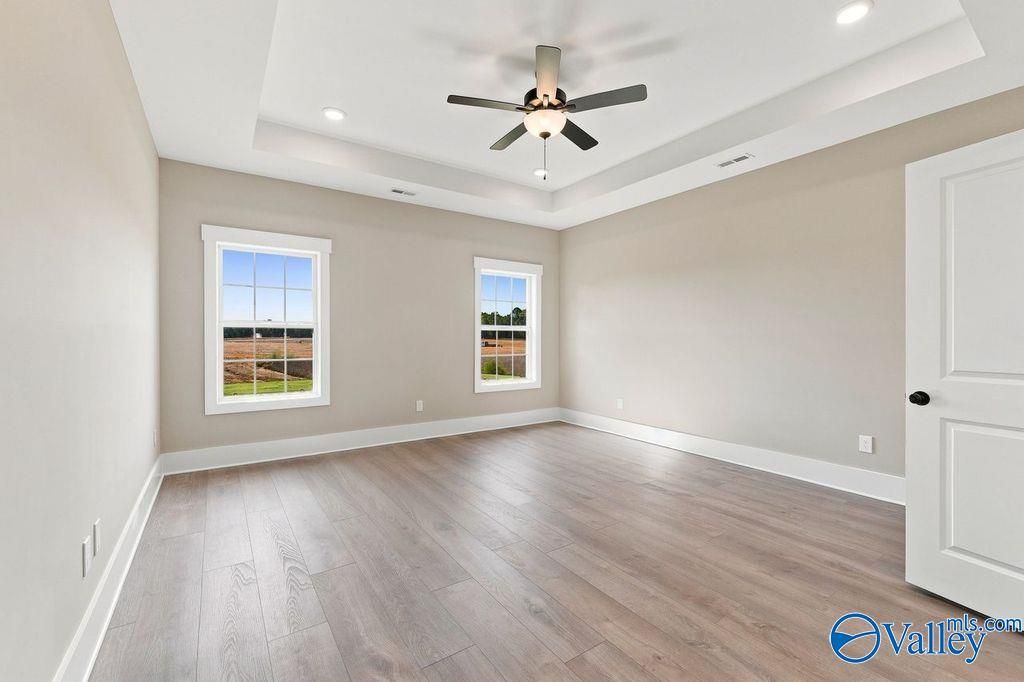 Spacious bedroom with tray ceiling and wood-style flooring in The Rockford floor plan by Davidson Homes in Hartselle, AL.
