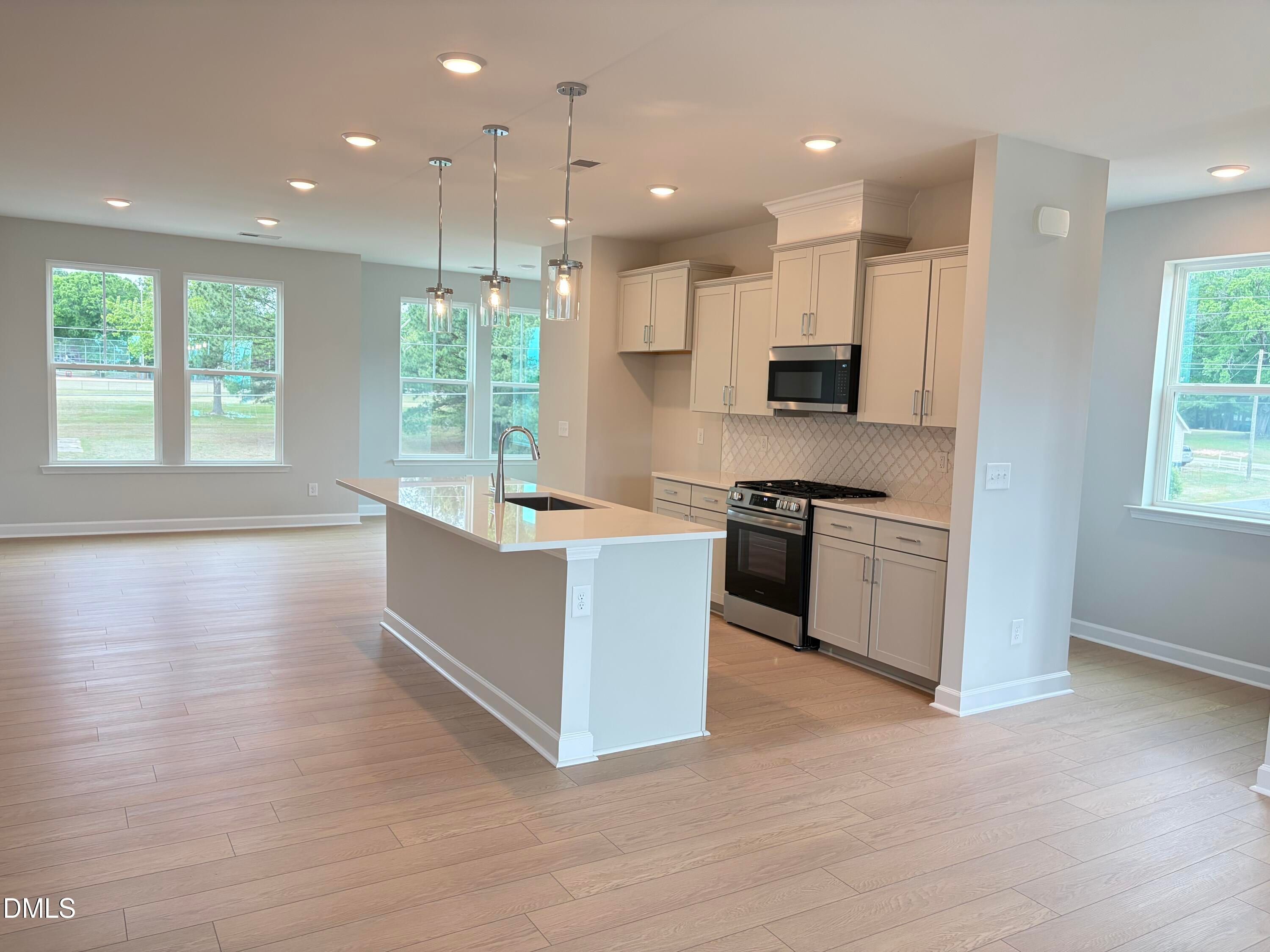 Open-concept kitchen with white shaker cabinets, stainless steel appliances, quartz island, and large windows in Davidson Homes The Mitchell, Knightdale, NC