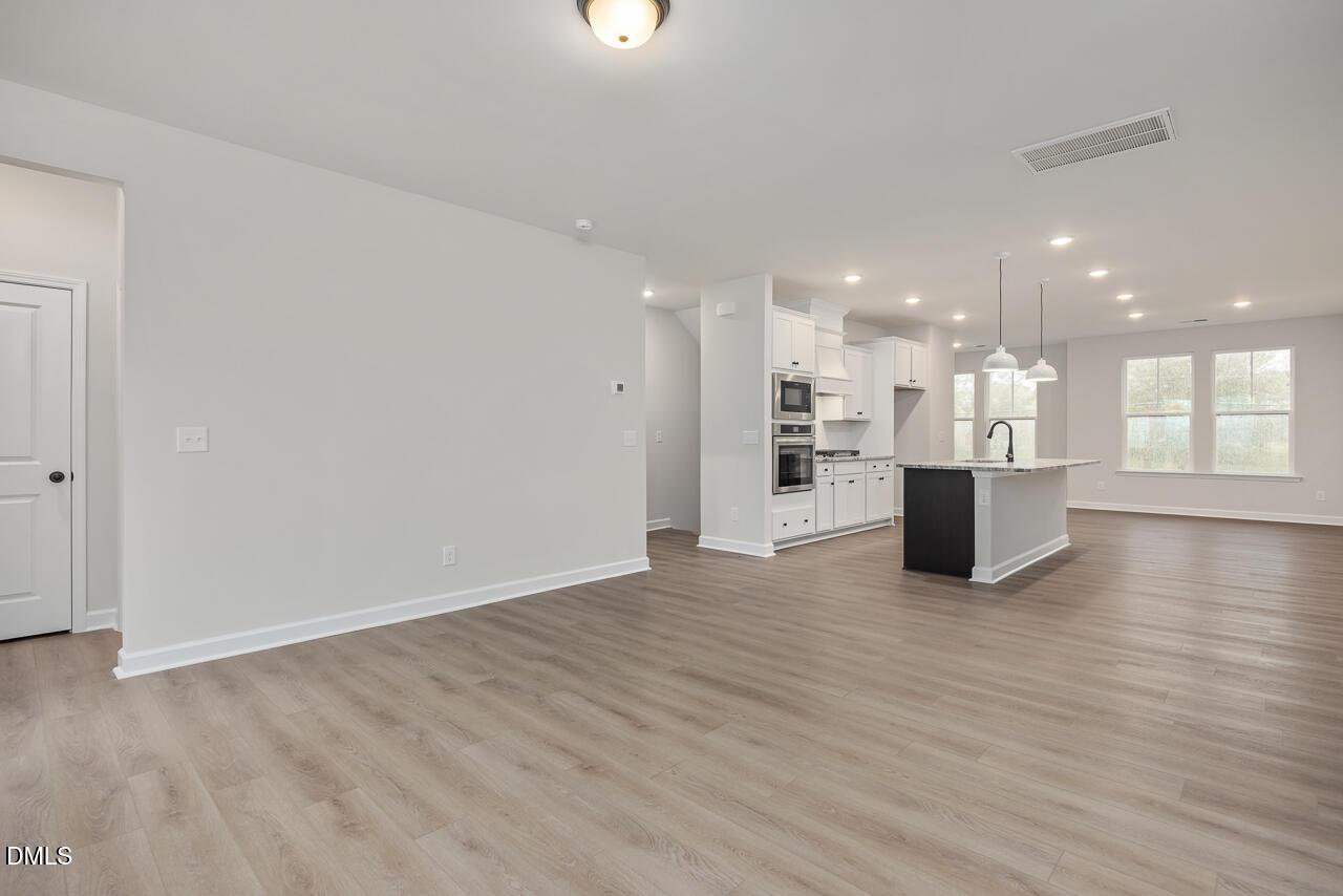 Modern open kitchen featuring white shaker cabinets, black island with sink, stainless double ovens, pendant lights, and hardwood floors in Davidson Homes The Mitchell, Knightdale, NC