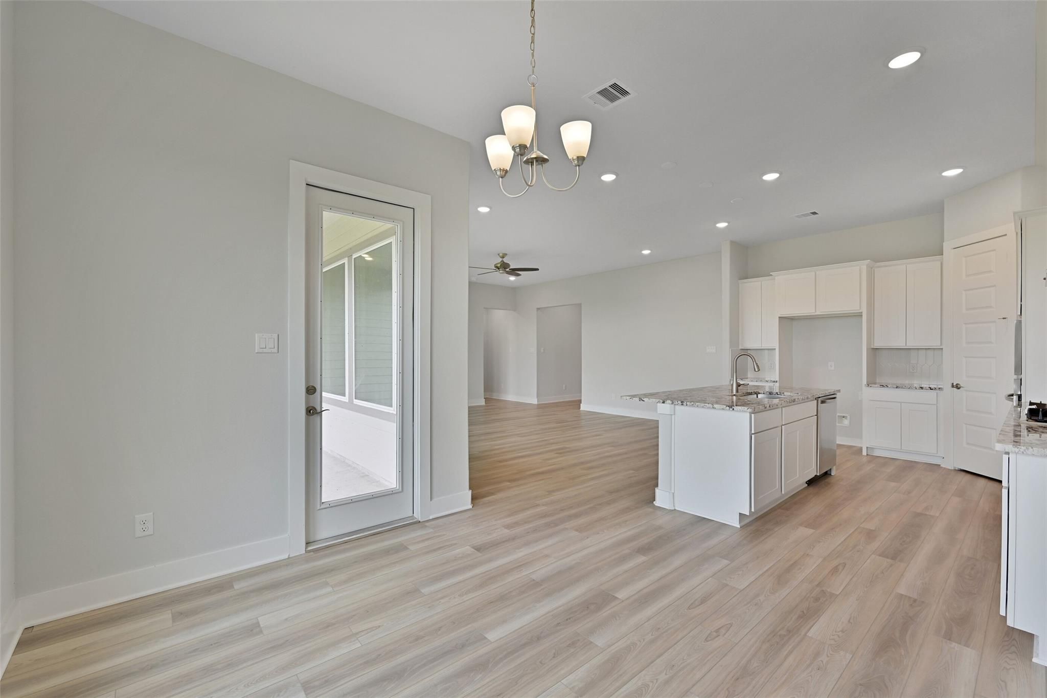 Open-concept kitchen-living space with white cabinets, granite island sink, light wood floors, chandelier, and French door to patio in Davidson Homes The Edward A, Lago Mar, Texas City