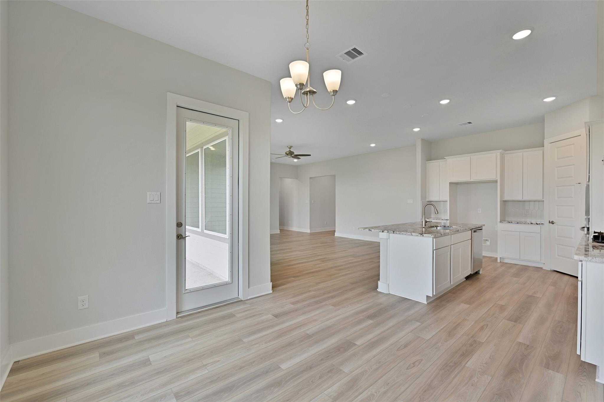 Open-concept kitchen-living space with white cabinets, granite island sink, light wood floors, chandelier, and French door to patio in Davidson Homes The Edward A, Lago Mar, Texas City