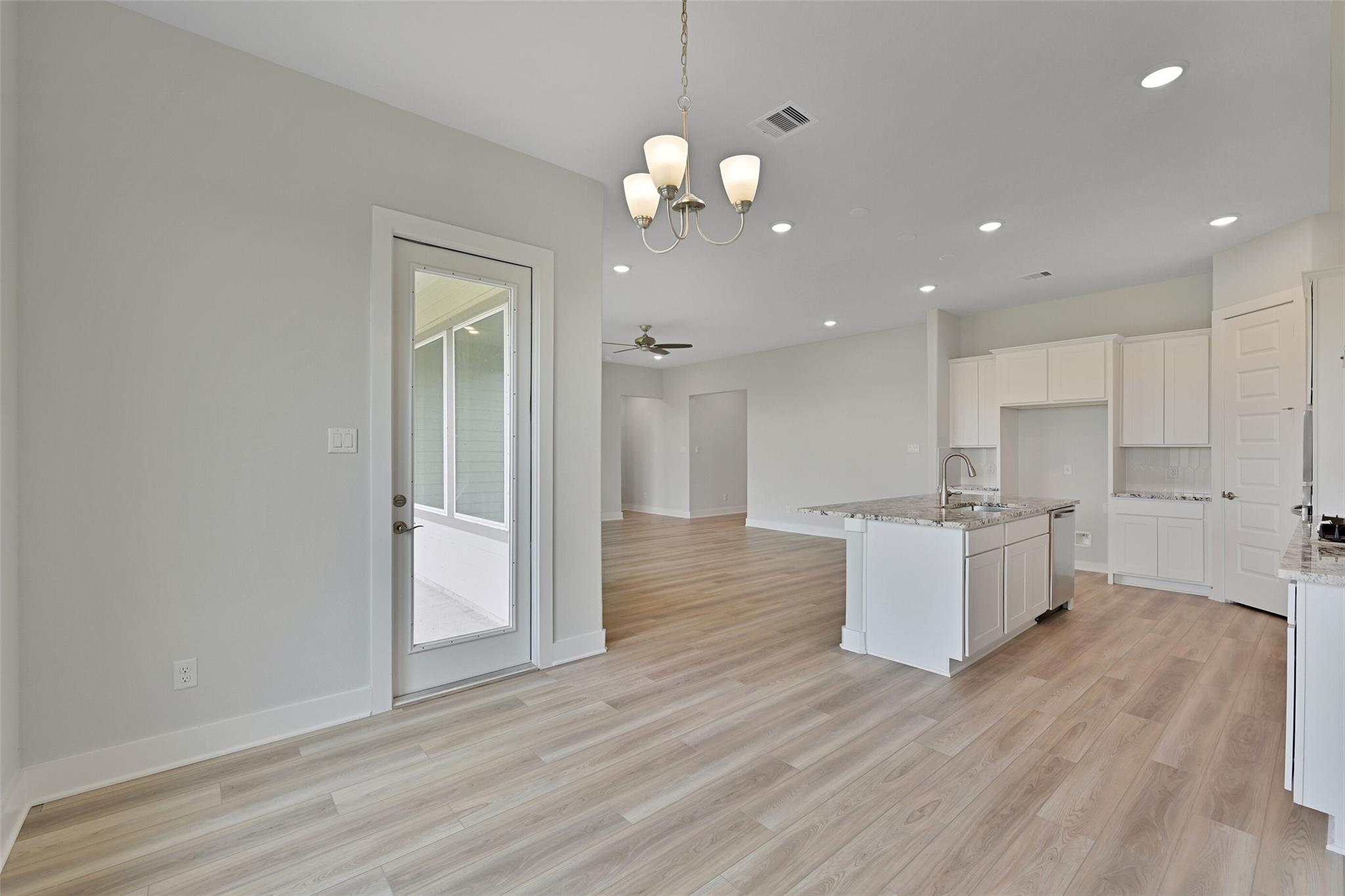 Open-concept kitchen-living space with white cabinets, granite island sink, light wood floors, chandelier, and French door to patio in Davidson Homes The Edward A, Lago Mar, Texas City