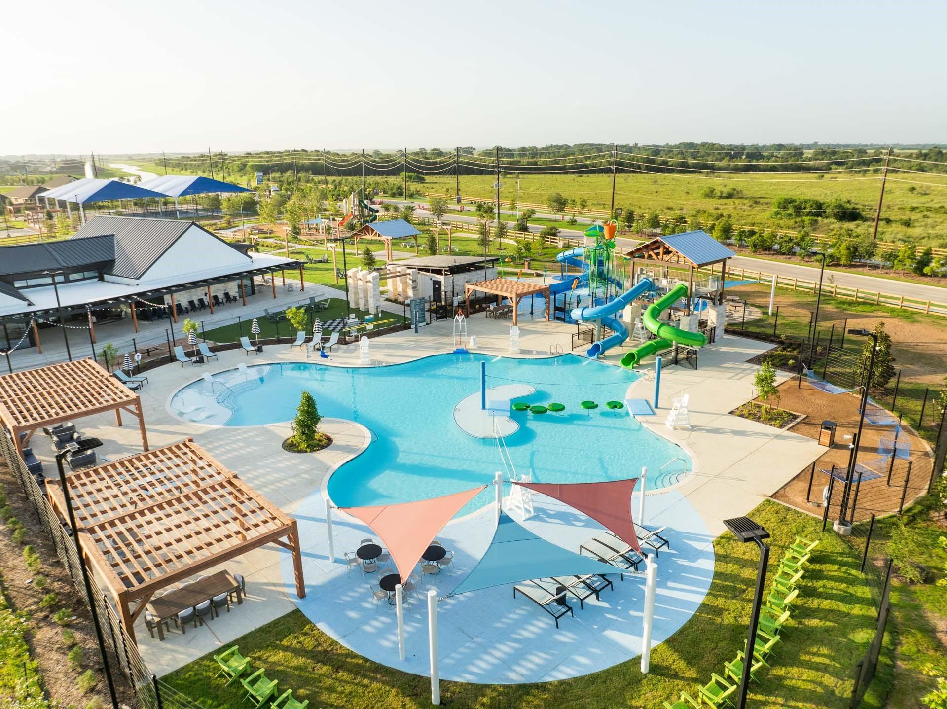 Resort-style community pool with water slides and clubhouse at Emberly by Davidson Homes in Beasley, Texas
