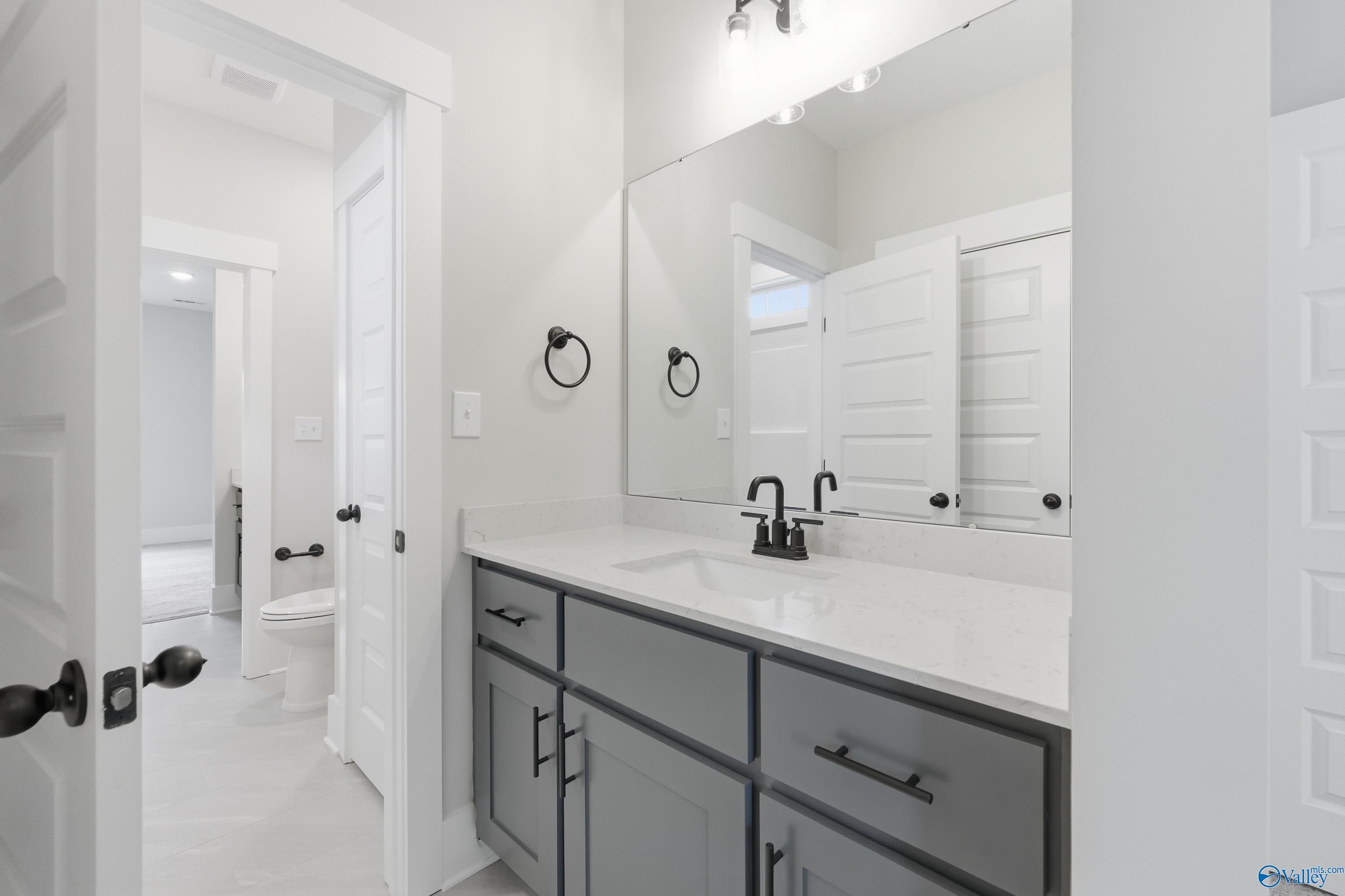 Modern bathroom with gray vanity, white quartz countertop, black faucet, and large mirror in Davidson Homes The Finleigh, Meridianville AL
