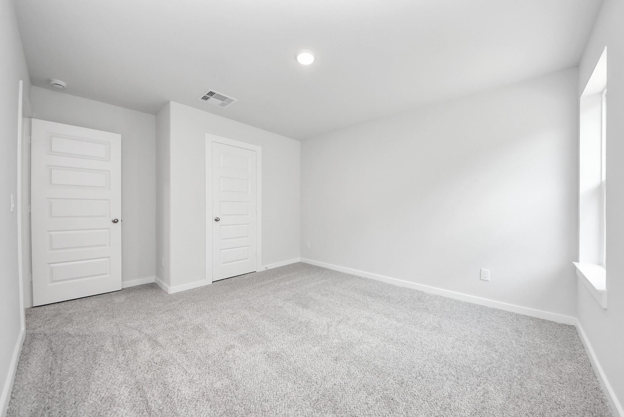 Bright, carpeted bedroom with neutral walls in The Sabine E floor plan at Windmill Estates in Magnolia, Texas.