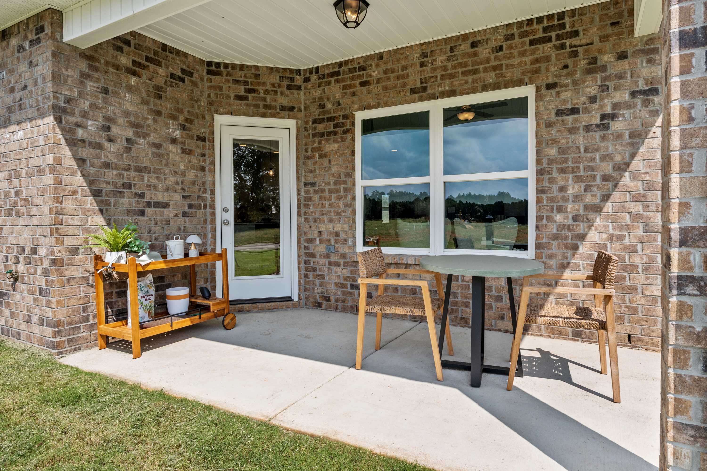 Covered patio at Wood Trail in Toney Alabama with brick home exterior, round table, wooden chairs, and potted plants