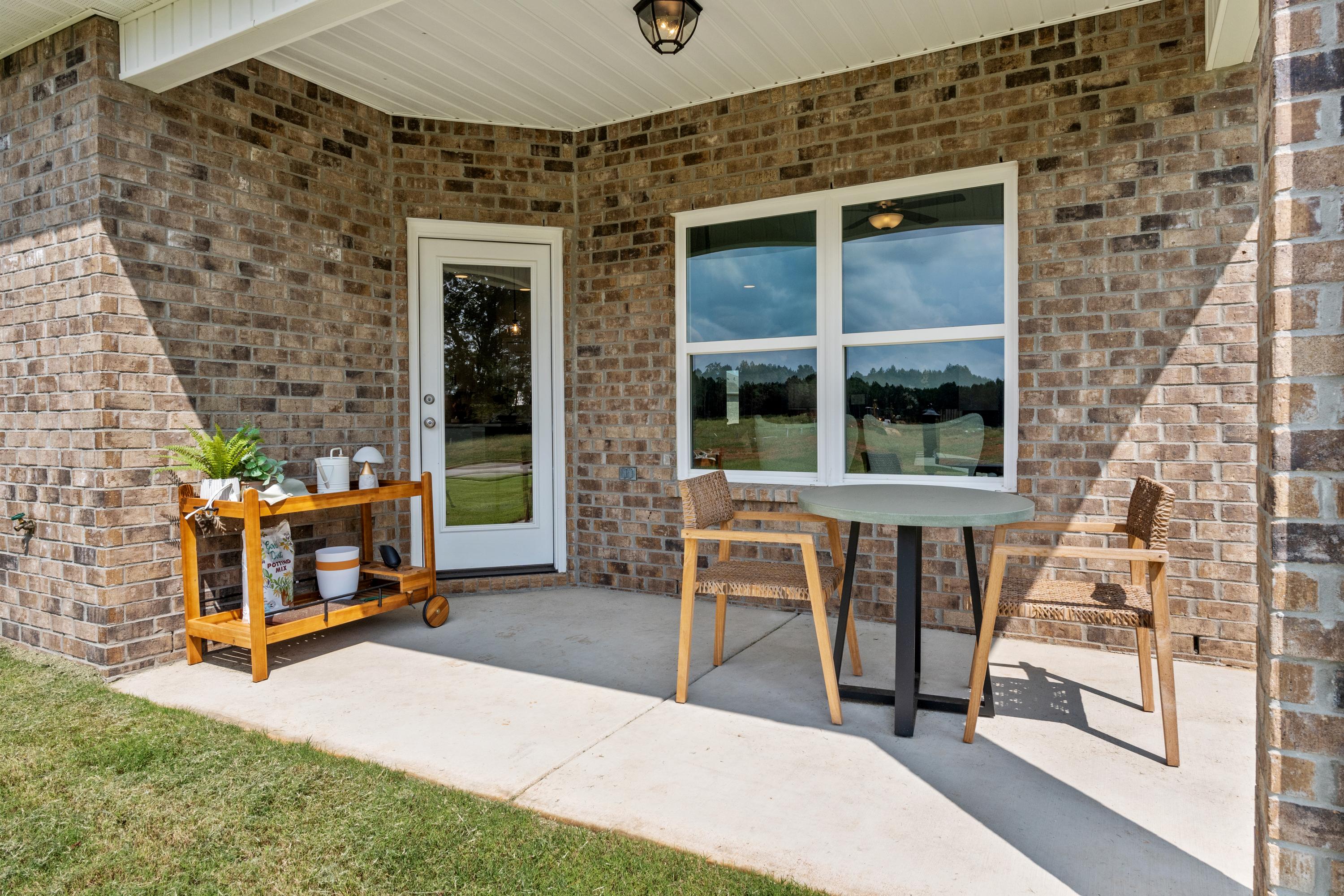 Covered patio at Wood Trail in Toney Alabama with brick home exterior, round table, wooden chairs, and potted plants