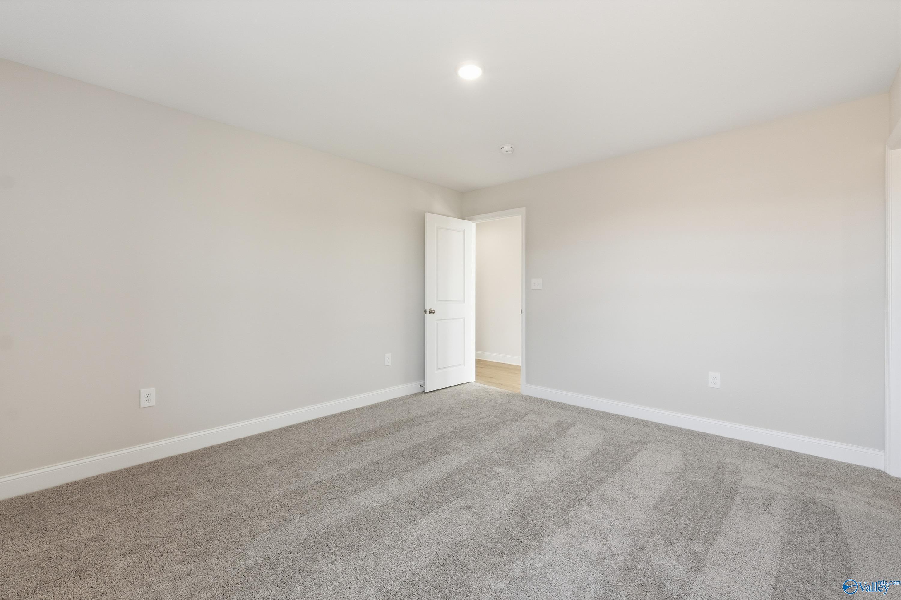 Empty secondary bedroom featuring beige walls, gray carpet, and open door in Davidson Homes The Butler, New Market, Alabama