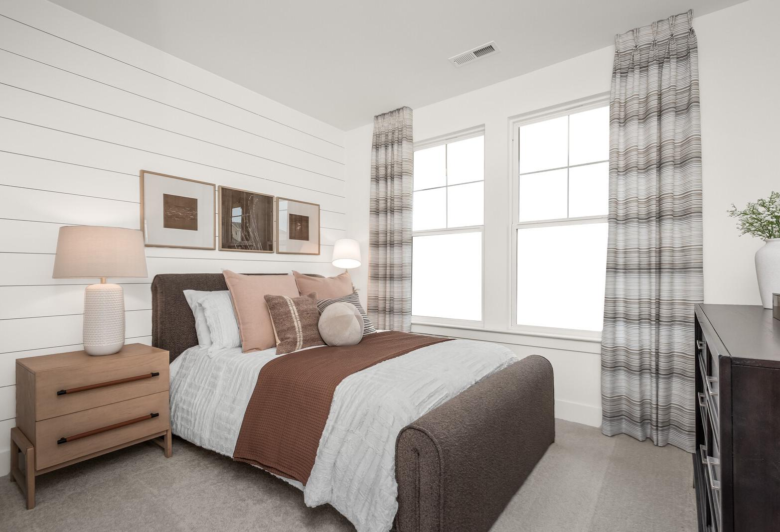 Spacious secondary bedroom in The Ridgeport E with white shiplap walls, upholstered bed, neutral bedding, and large curtained windows