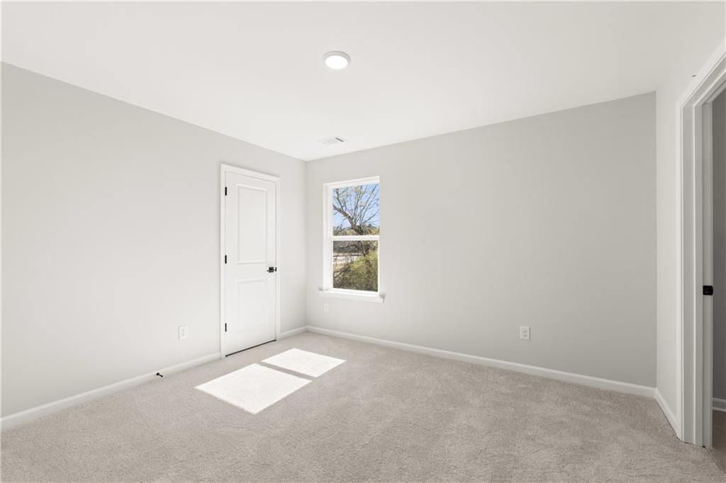 Bright secondary bedroom with light gray walls, carpet floor, and window light in Davidson Homes The Hickory B, Winder, Georgia