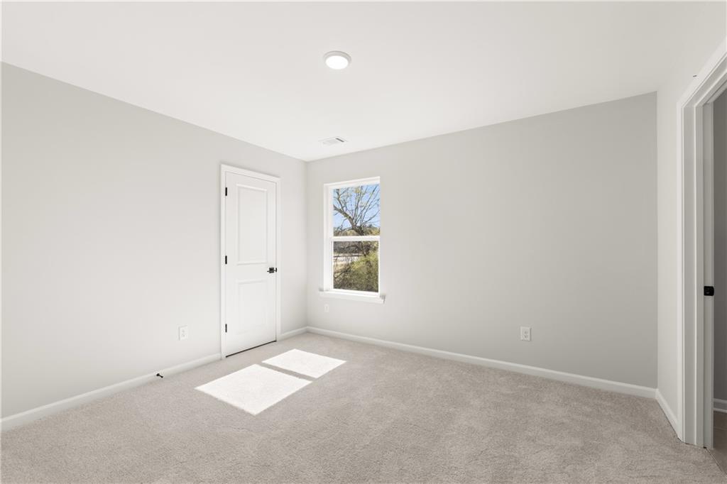 Bright secondary bedroom with light gray walls, carpet floor, and window light in Davidson Homes The Hickory B, Winder, Georgia