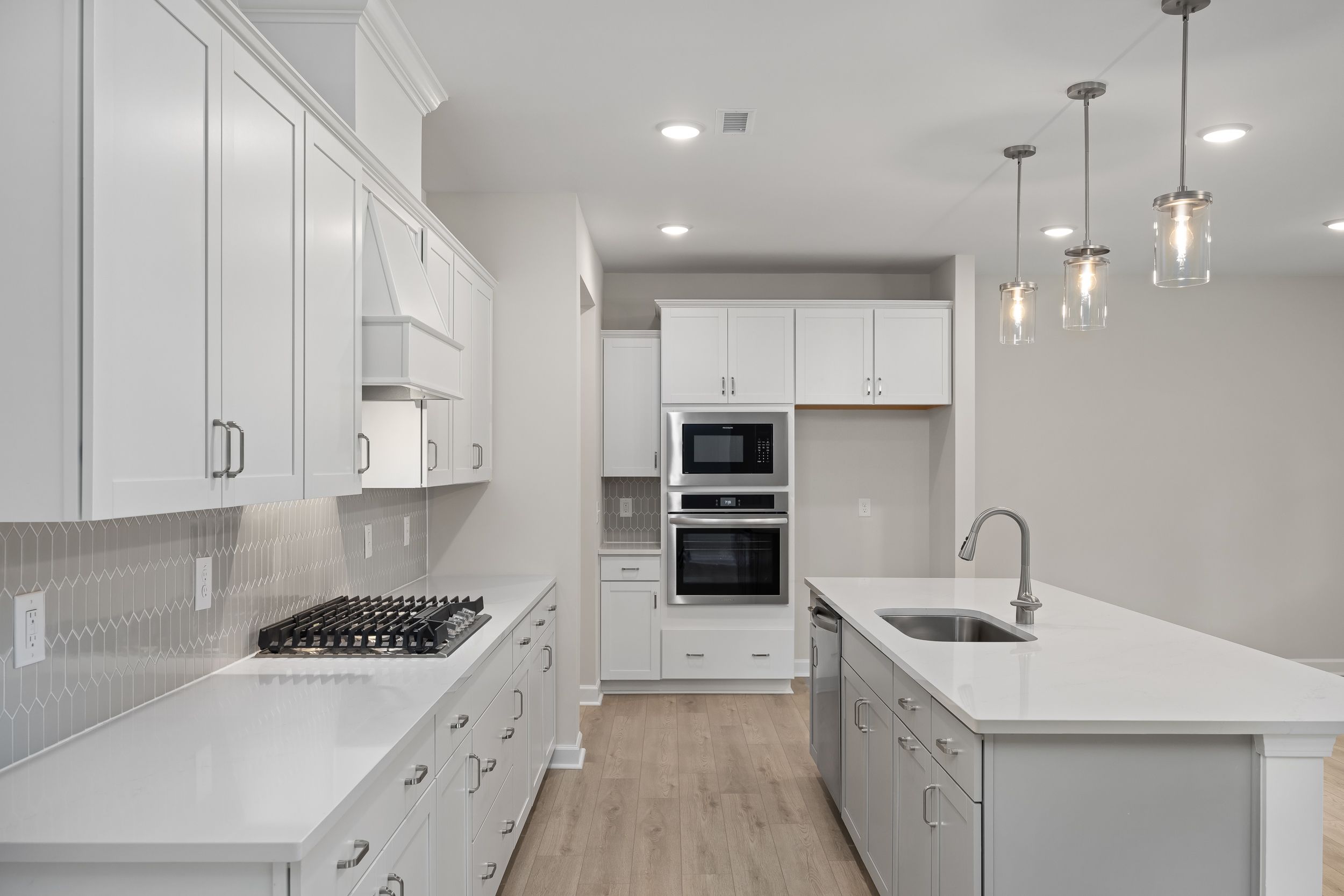 Spacious gourmet kitchen in The Beech A with white shaker cabinets, large quartz island, gas cooktop, double ovens, and subway tile backsplash