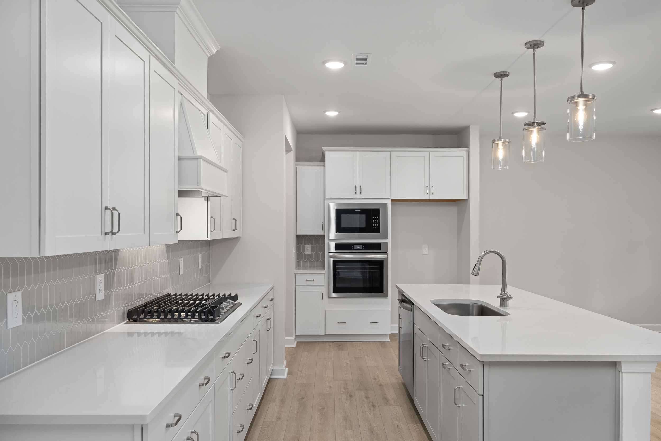 Modern white kitchen in The Beech C featuring large island, gas range, double ovens, and pendant lights