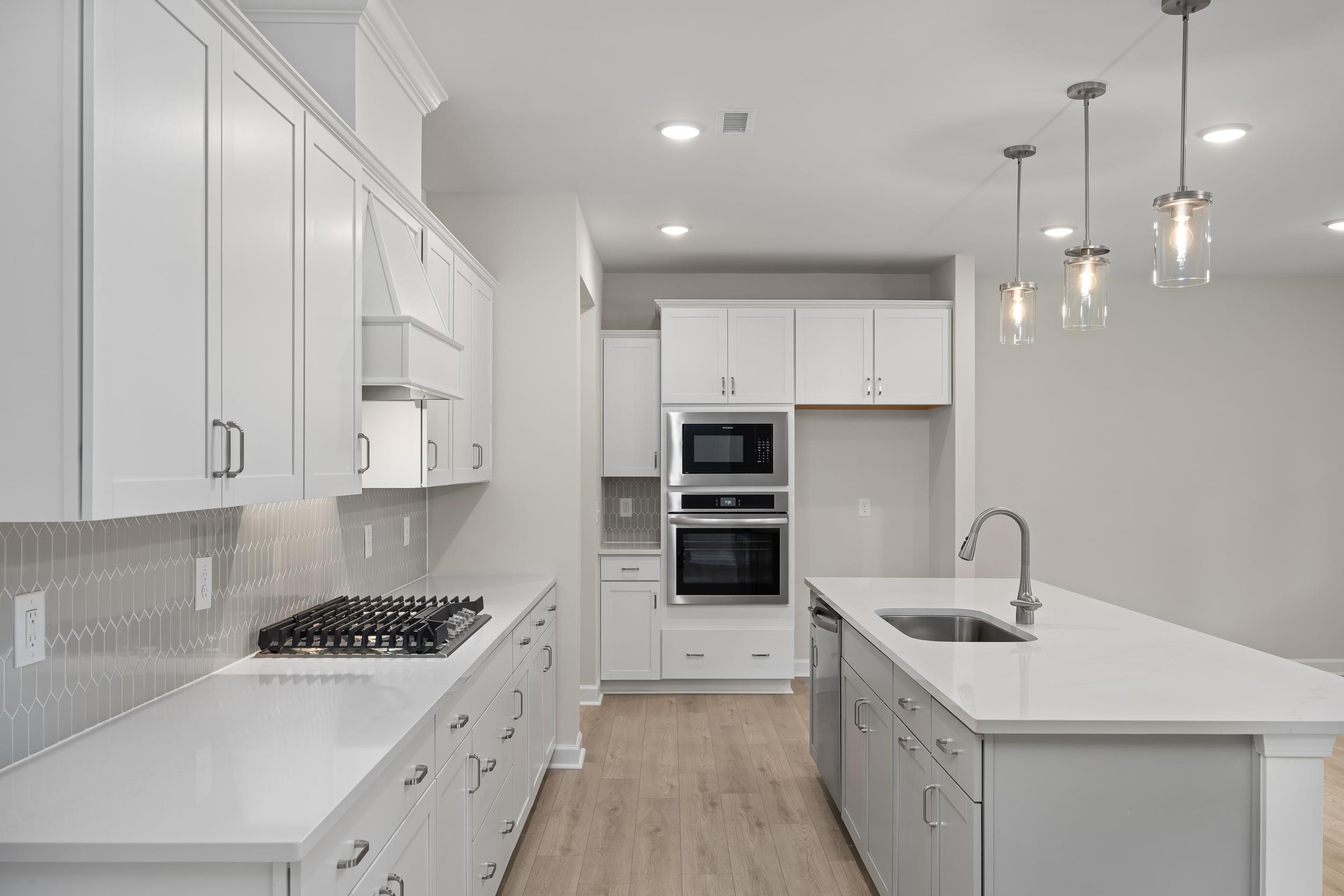 Spacious gourmet kitchen in The Beech A with white shaker cabinets, large quartz island, gas cooktop, double ovens, and subway tile backsplash