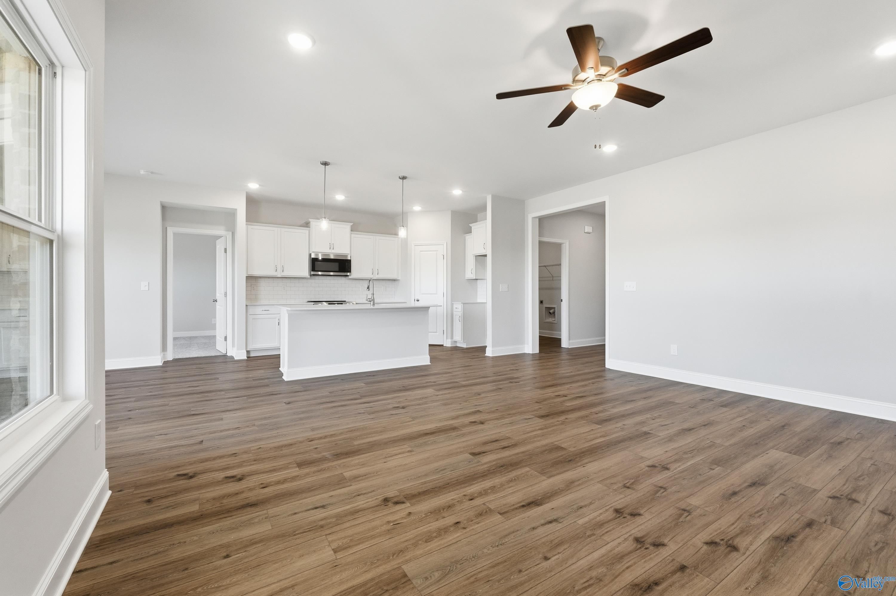 Open-concept living room and kitchen with hardwood floors, white cabinets, and ceiling fan in Davidson Homes The Everett, Harvest, Alabama