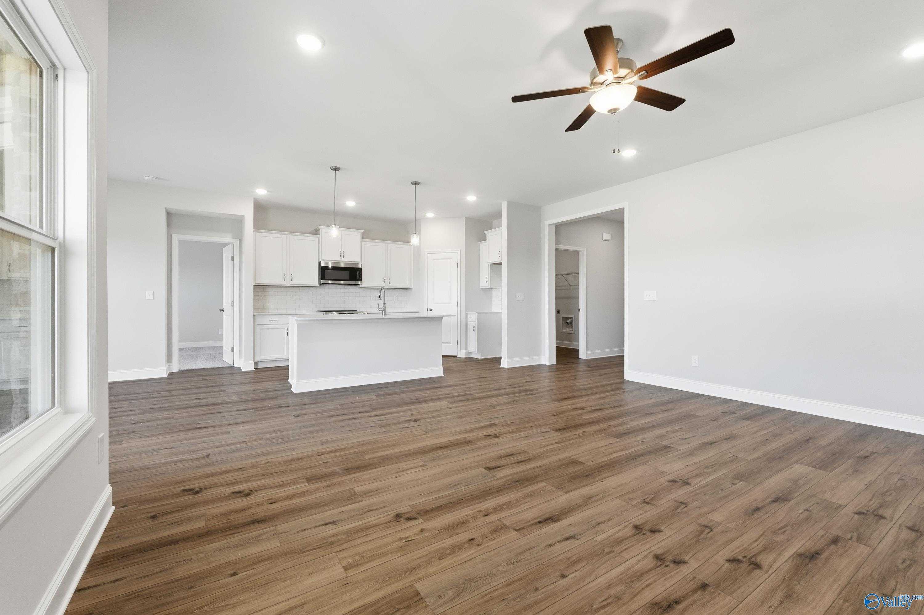 Open-concept living room and kitchen with hardwood floors, white cabinets, and ceiling fan in Davidson Homes The Everett, Harvest, Alabama