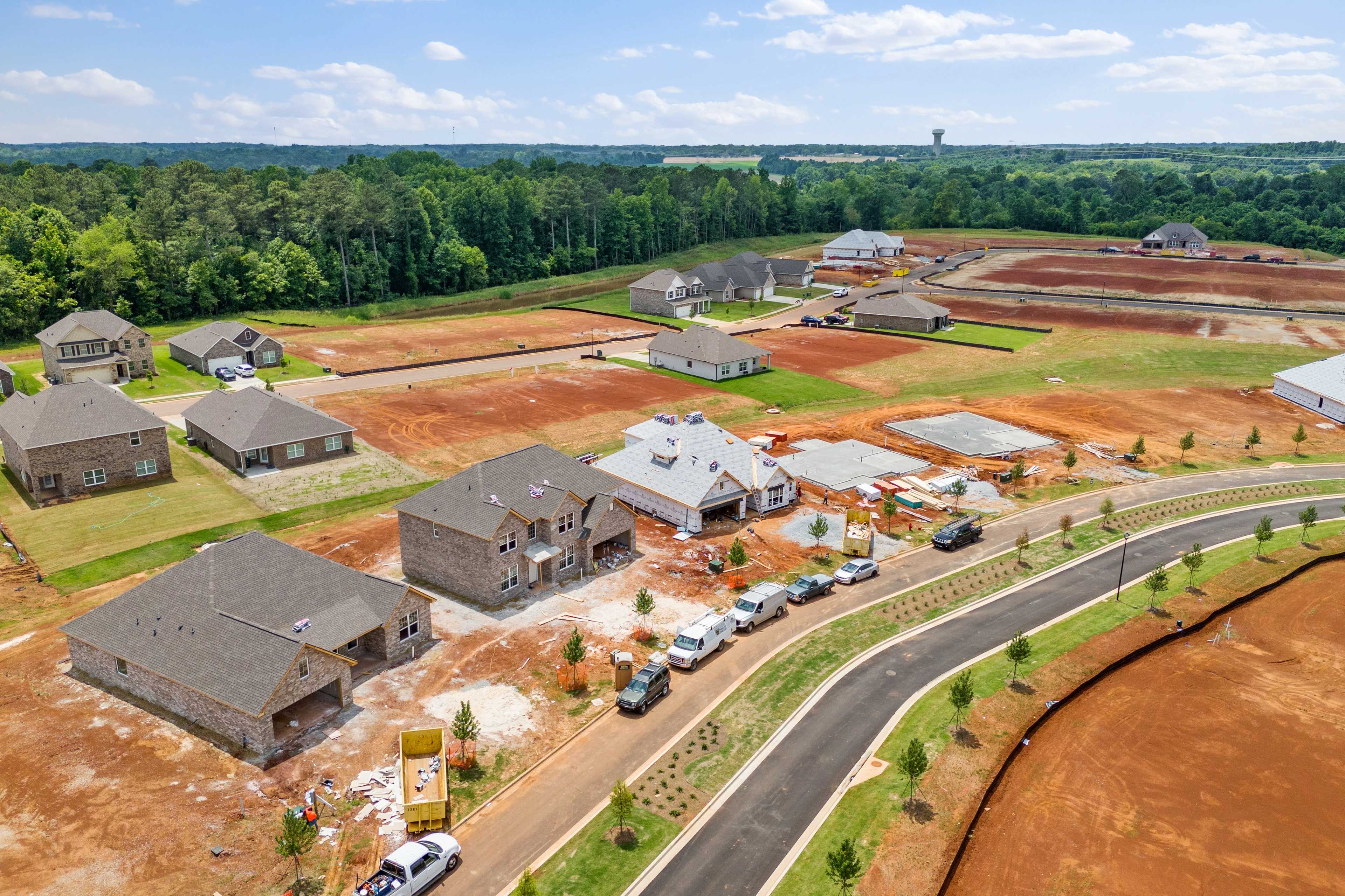 Aerial view of Creekside neighborhood under construction in Harvest Alabama with new brick homes, red dirt lots, and surrounding pine trees