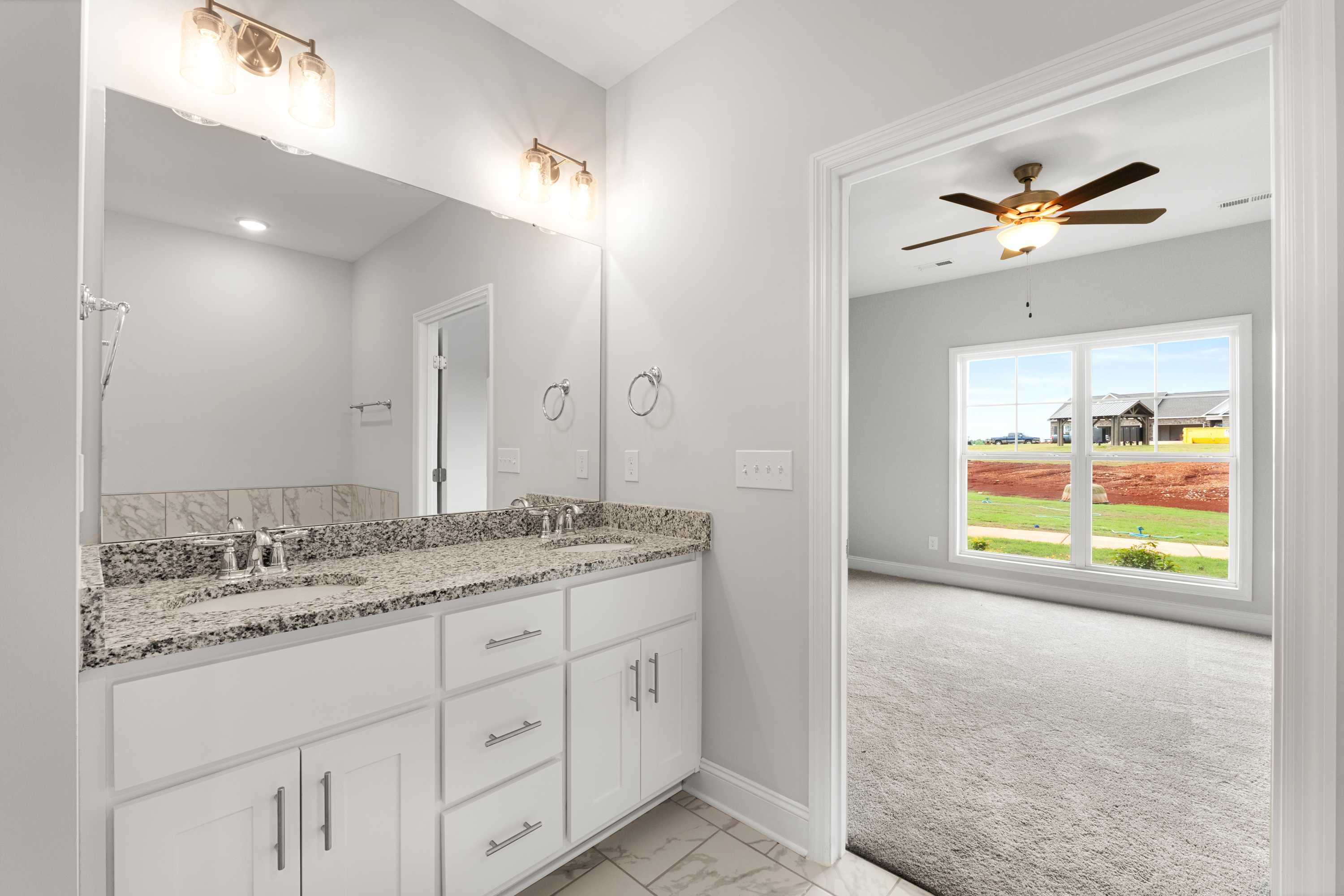 Master bathroom in The Copeland B showcasing double vanity with granite countertop, white cabinets, and adjacent carpeted bedroom