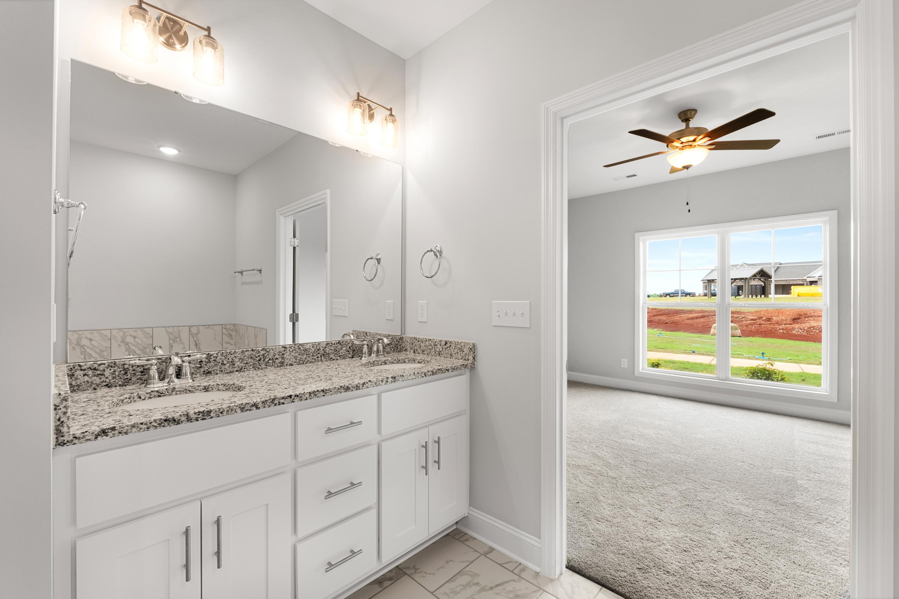 Spacious master bathroom in The Copeland C with double granite vanity, white shaker cabinets, large mirror, and adjacent bedroom view