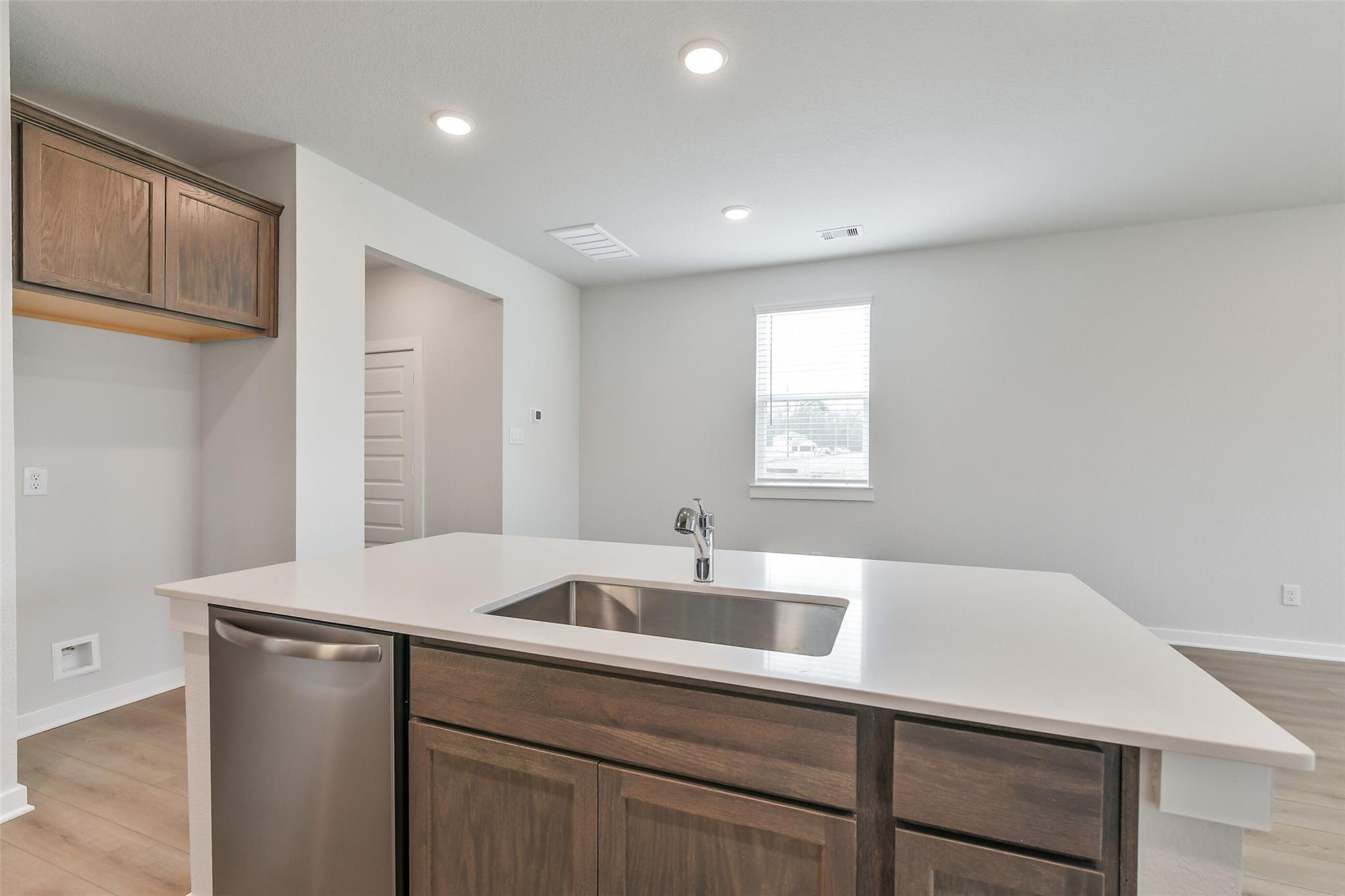 Modern kitchen with central island, stainless sink, dishwasher, and shaker cabinets in Davidson Homes The Brazos E, Cleveland TX