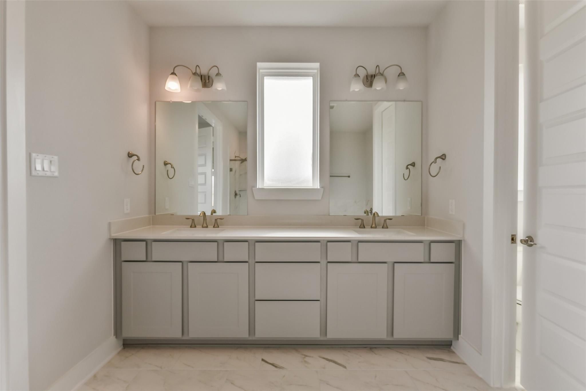 Modern master bathroom with double gray vanity, mirrors, sconce lights, and window in Davidson Homes The George A, Lago Mar, Texas City