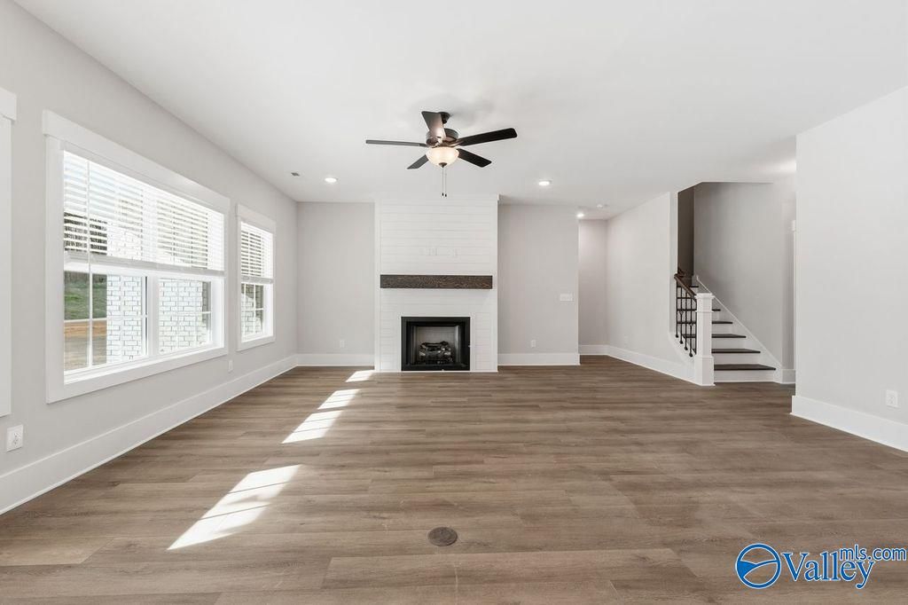 Spacious living room with white brick fireplace, hardwood floors, large windows, and ceiling fan in Davidson Homes The Rockford, Hartselle, Alabama