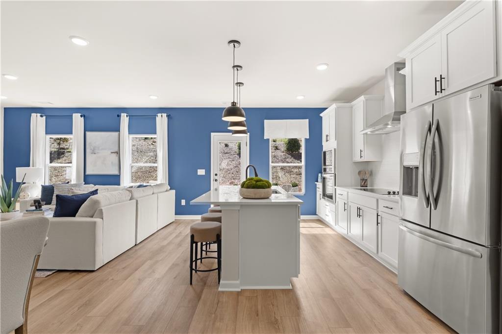 Open-concept kitchen with white island, stainless fridge, pendant lights, and living room blue accent wall in Davidson Homes The Burton C, Canton, Georgia