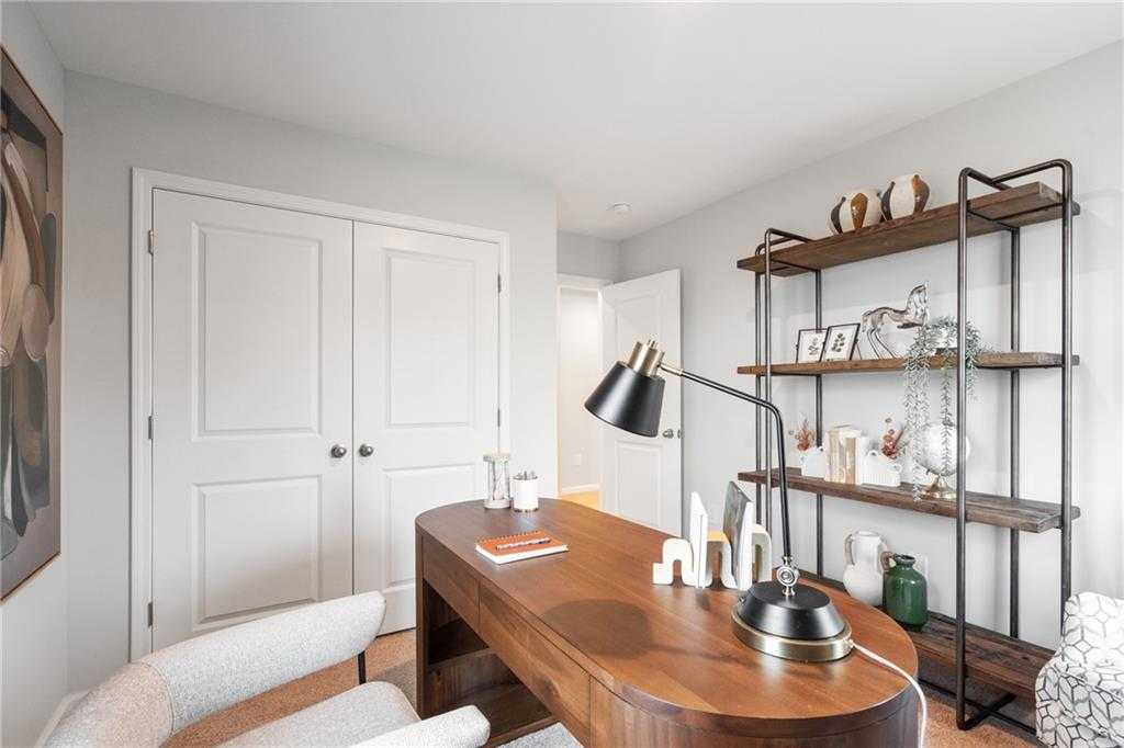 Modern home office with wooden desk, ergonomic gray chair, and metal bookshelf in Davidson Homes The Wilmington B, Emerson, GA