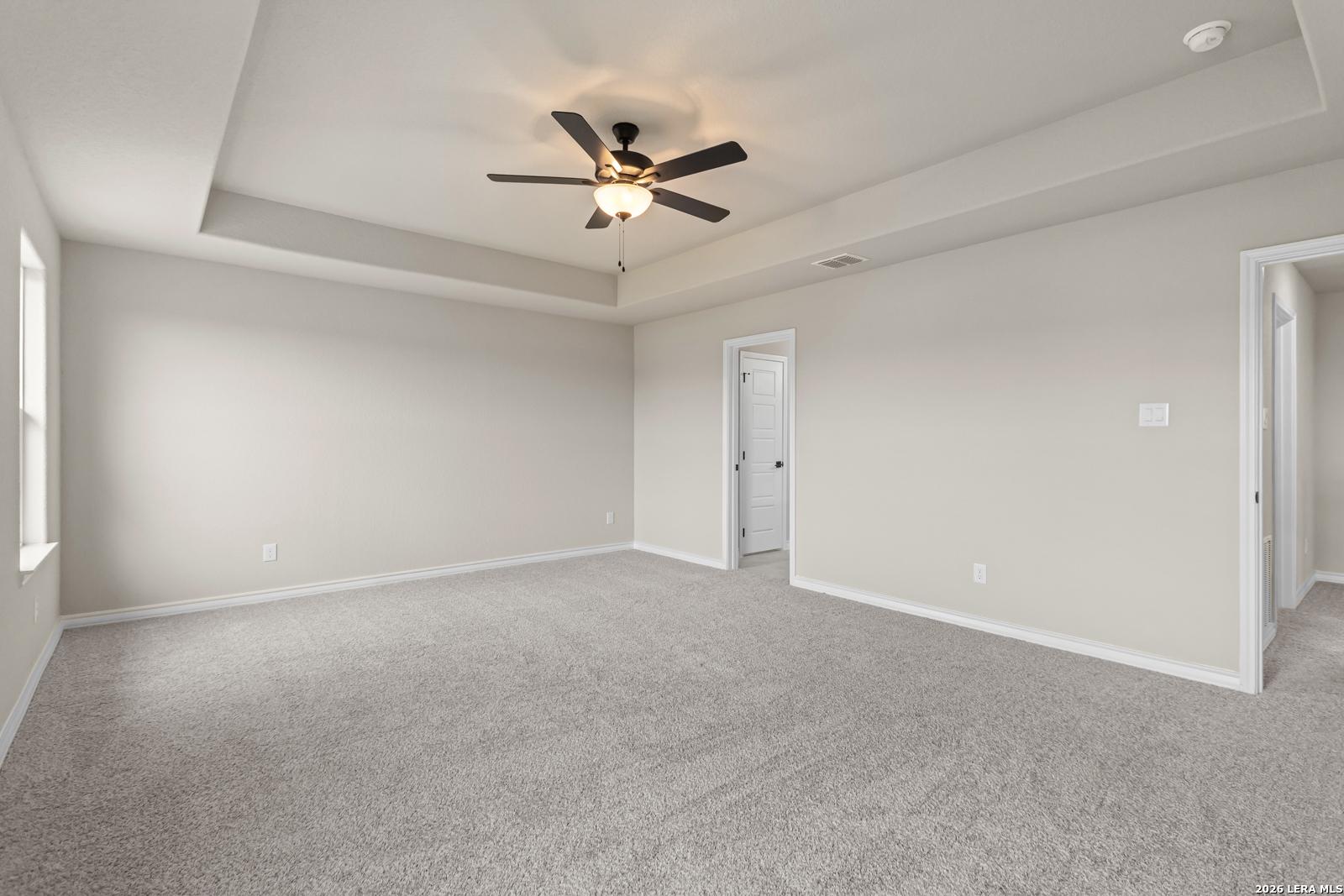 Spacious bedroom with tray ceiling and ceiling fan in The Danbury H floor plan at The Reserve at Potranco Oaks, TX.
