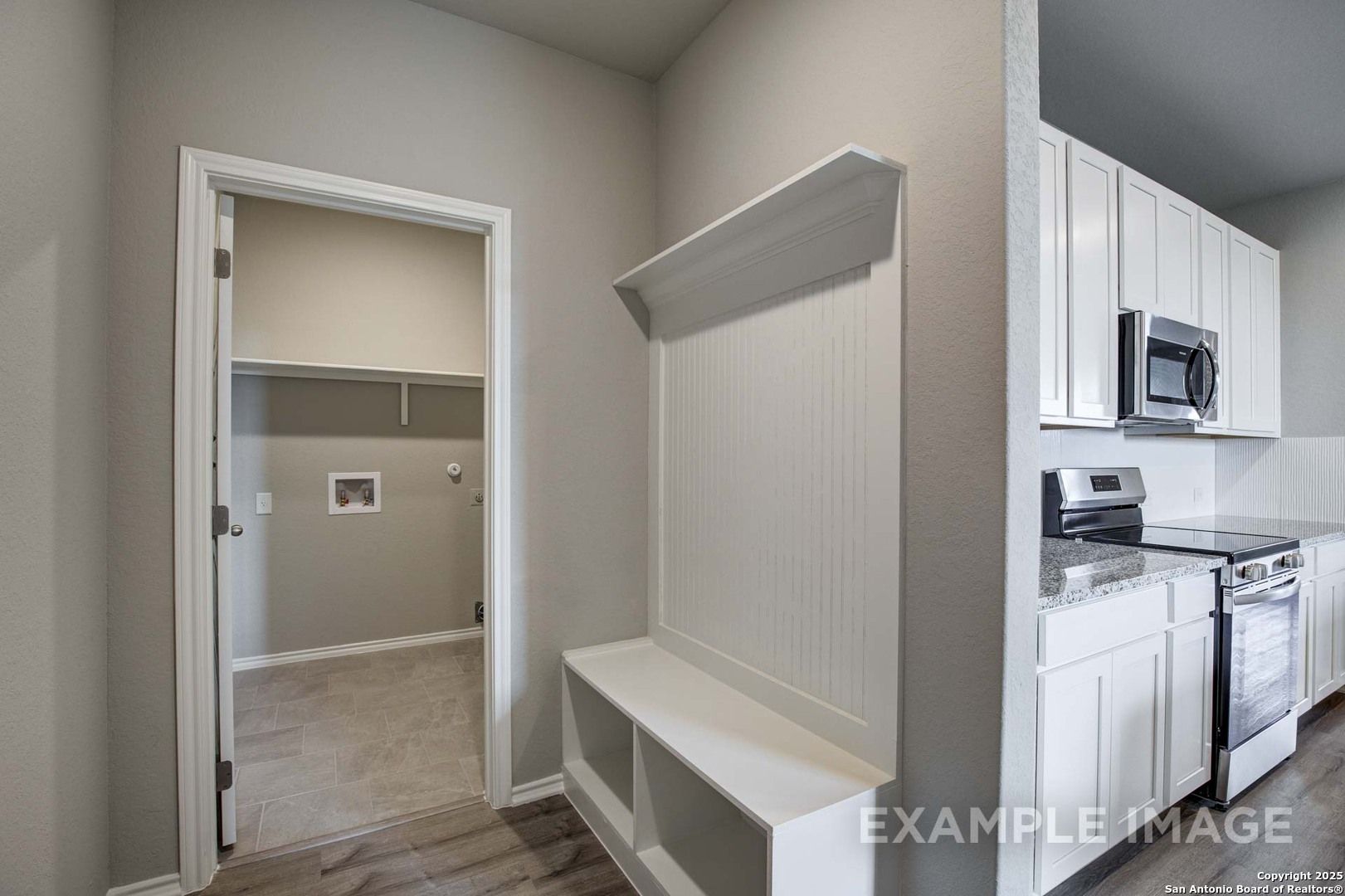 Functional mudroom with built-in bench, hooks, and laundry access beside white cabinet kitchen in Davidson Homes Blanco C, San Antonio