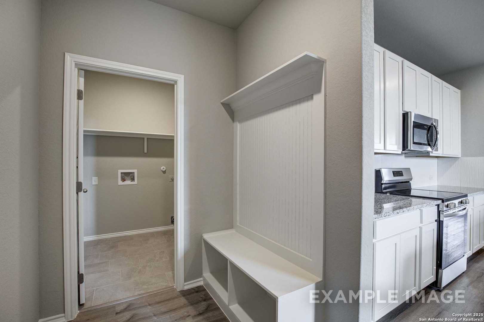 Functional mudroom with built-in bench, hooks, and laundry access beside white cabinet kitchen in Davidson Homes Blanco C, San Antonio