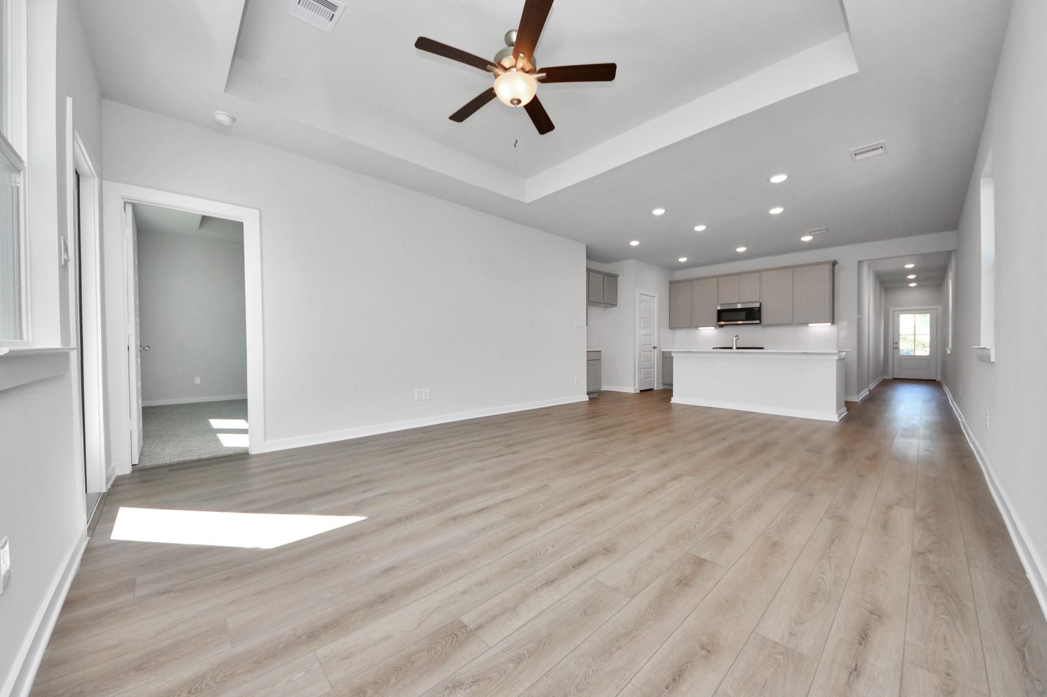 Open-concept living room and kitchen with tray ceiling in The Colorado G floor plan at Emberly in Beasley, Texas.