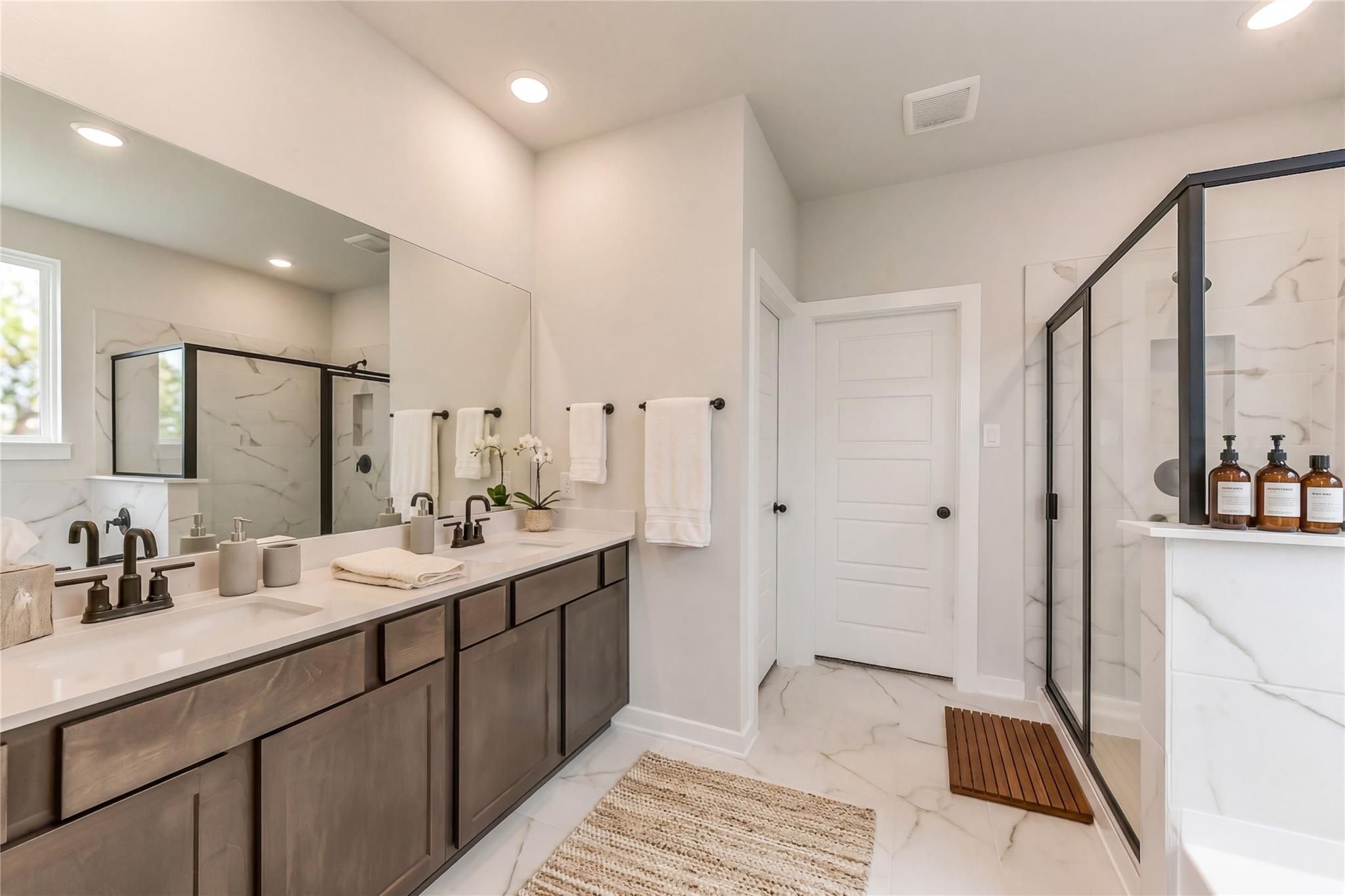 Modern master bathroom with double quartz vanity, bronze faucets, glass shower, and marble tiles in Davidson Homes The Sequoia C, Crosby, Texas