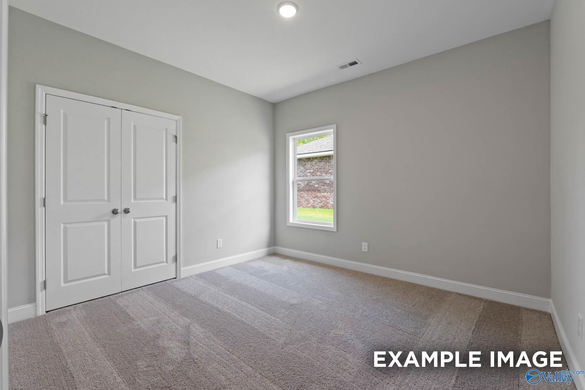 Spacious secondary bedroom with light gray walls, double closet doors, and backyard window in The Everett floor plan, Meridianville, Alabama