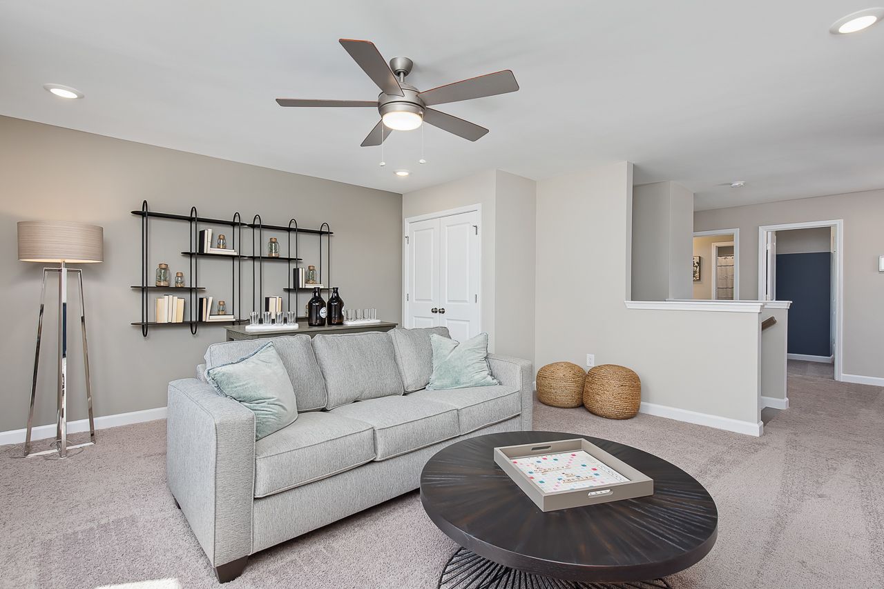 Cozy loft living area at Woodland Crossing in Zebulon, NC by Davidson Homes featuring a grey sofa and modern decor.