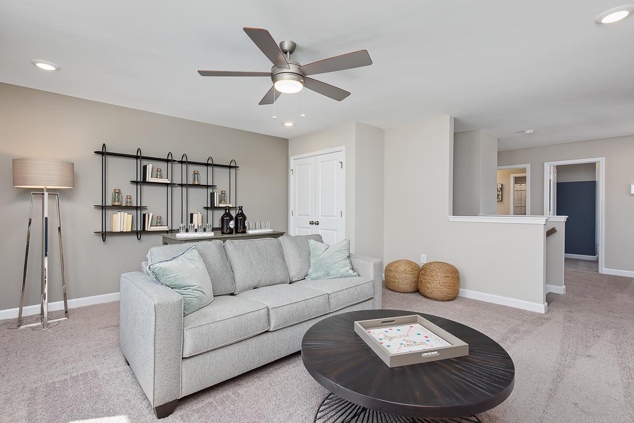 Cozy loft living area at Woodland Crossing in Zebulon, NC by Davidson Homes featuring a grey sofa and modern decor.