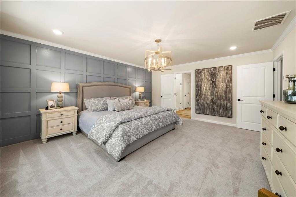 Elegant master bedroom with gray shiplap accent wall, king bed, chandelier, and walk-in closet in Davidson Homes The Hickory B, Riverwood, Dallas, Georgia