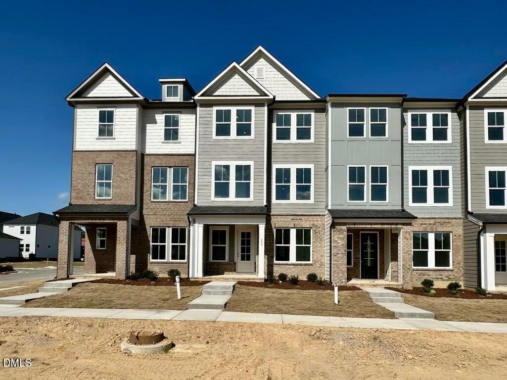 Modern 3-story townhomes featuring brick accents, white-gray siding, and covered porches in Forestville Yard Townhomes, Knightdale, NC