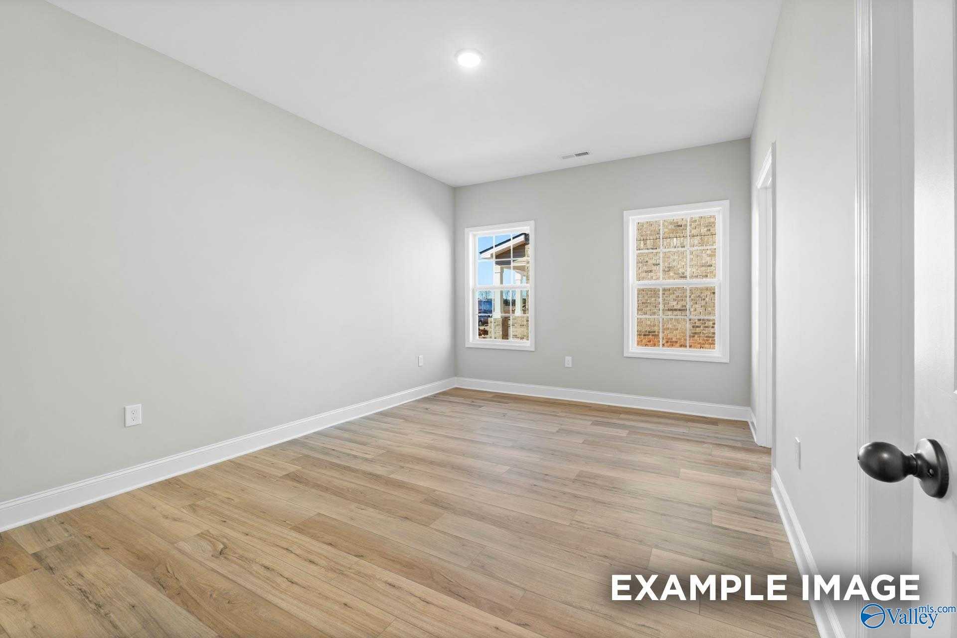 Bright empty bedroom with light gray walls, hardwood floors, and large window in Davidson Homes The Valencia, Meridianville, Alabama